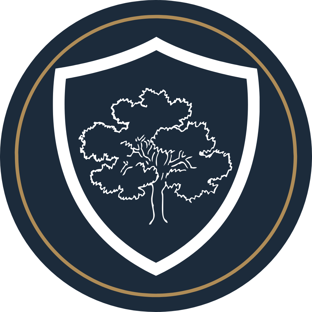 A dark-colored badge with a white shield outline, featuring a tree inside the shield, and a gold inner circle border around the badge.