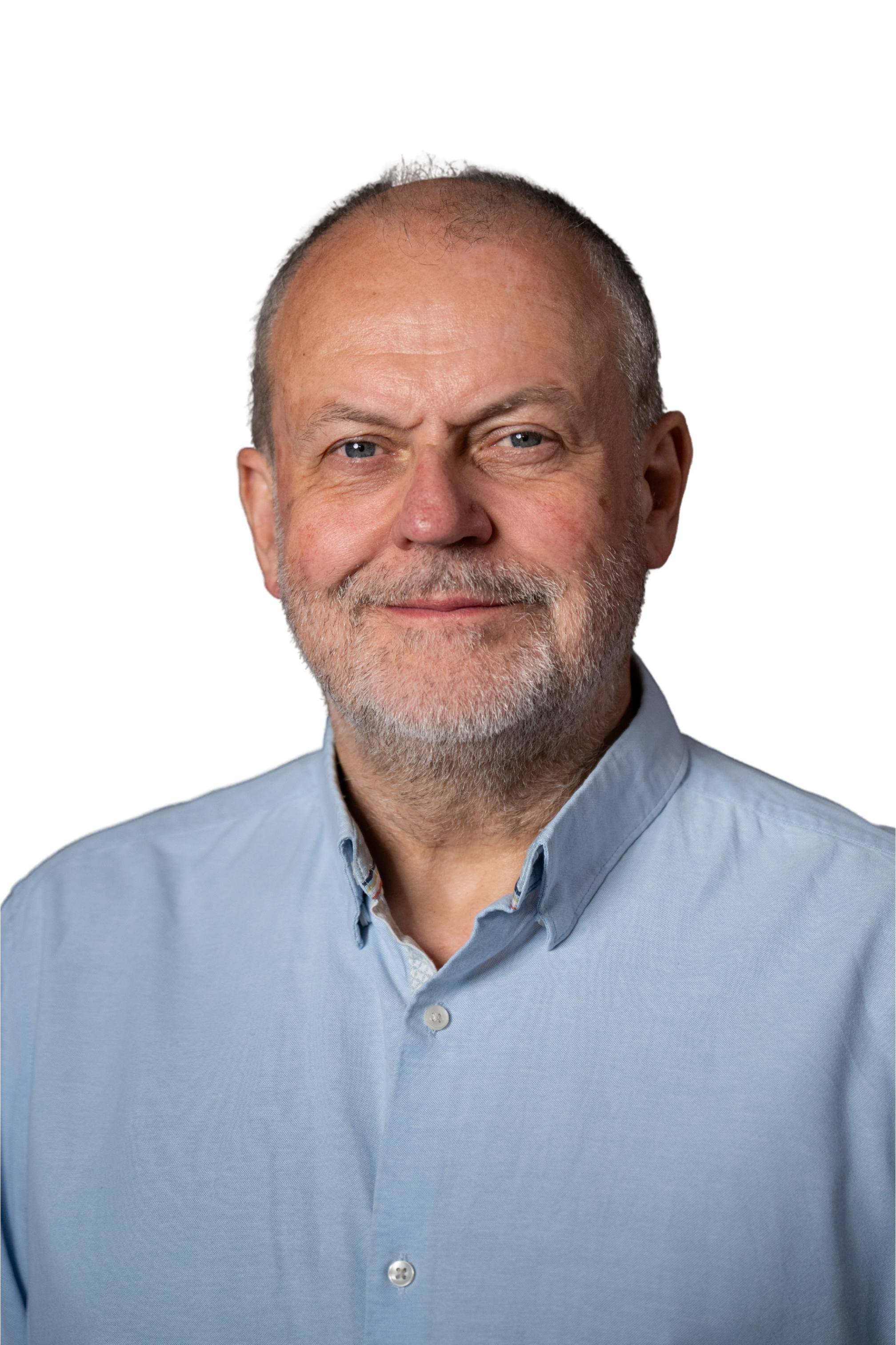 Close-up of a middle-aged man with short gray hair, blue eyes, a beard, wearing a light blue button-up shirt, smiling gently.