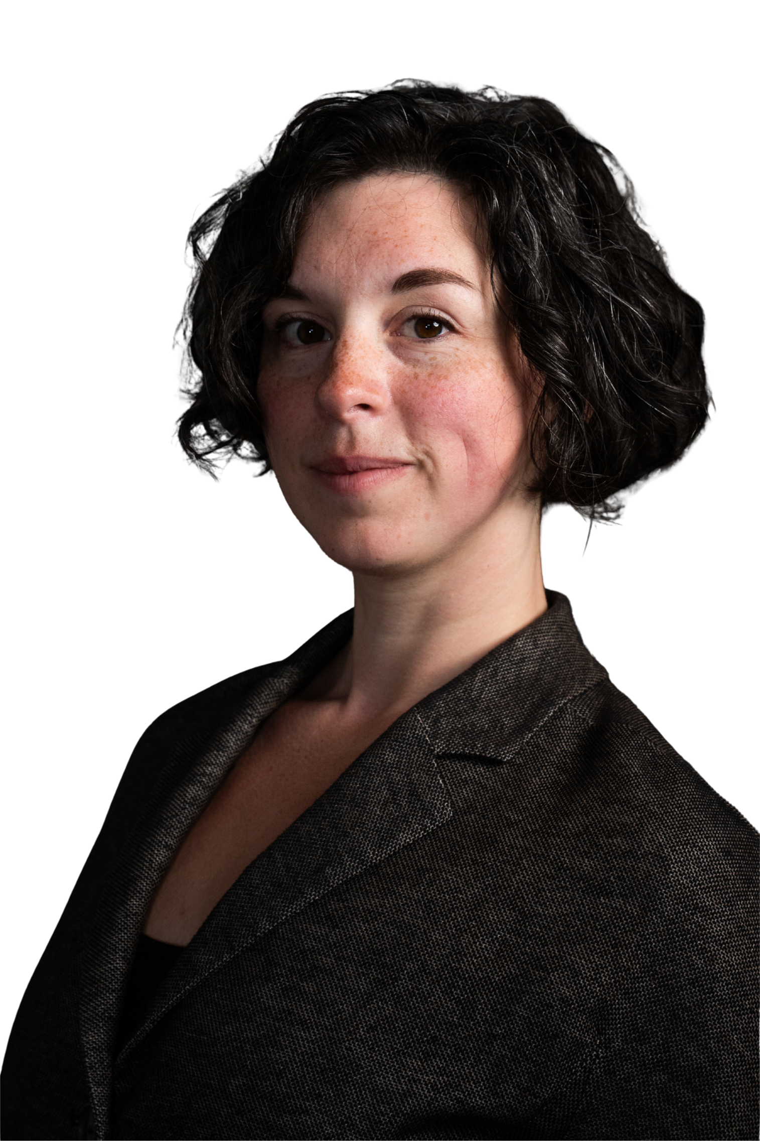 Portrait of a woman with dark curly hair, light skin with freckles, wearing a brown blazer, against a black background.