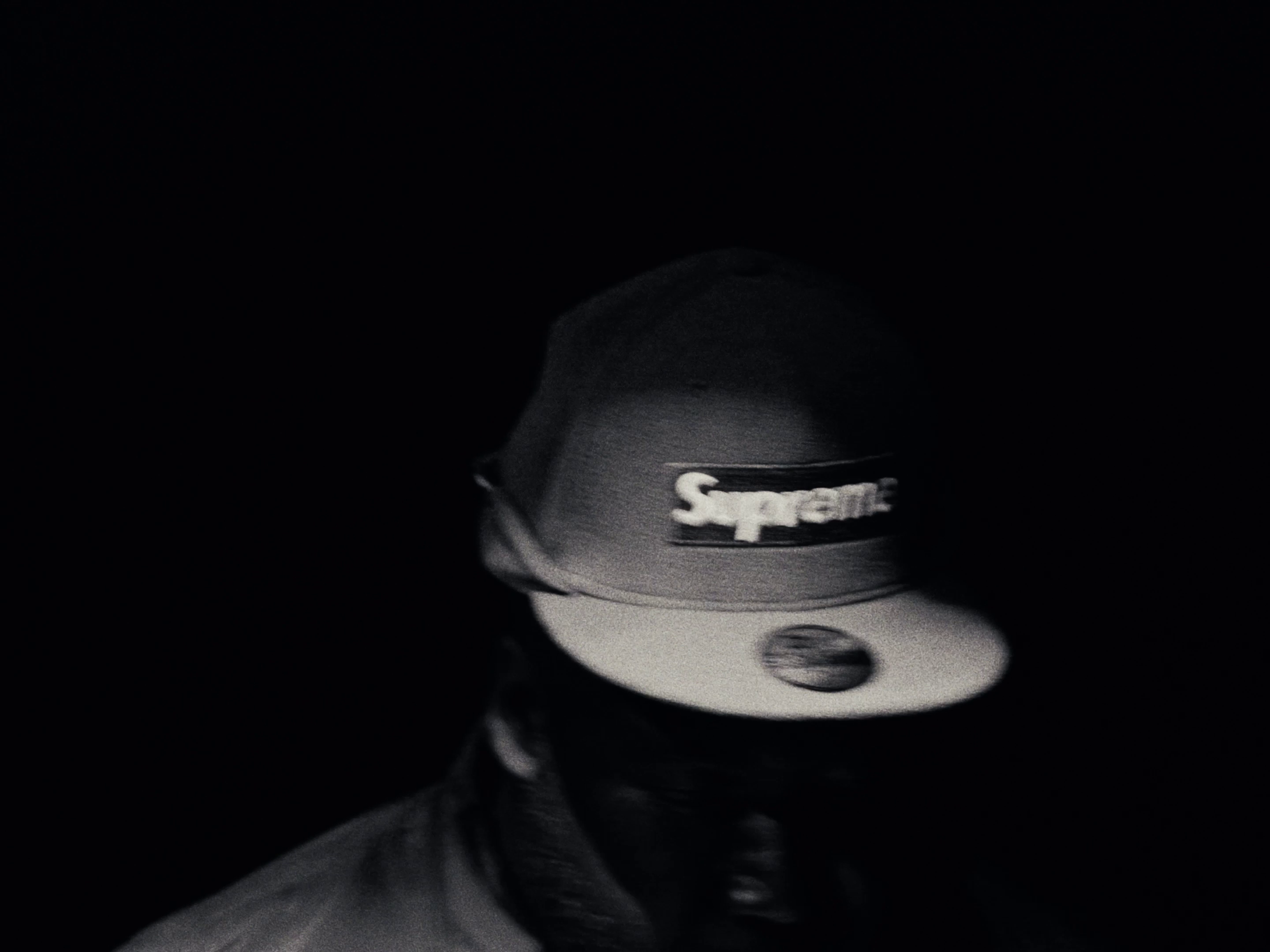 Close-up photo of a metallic object with the word 'Supreme' engraved or printed on it, partially illuminated against a dark background.