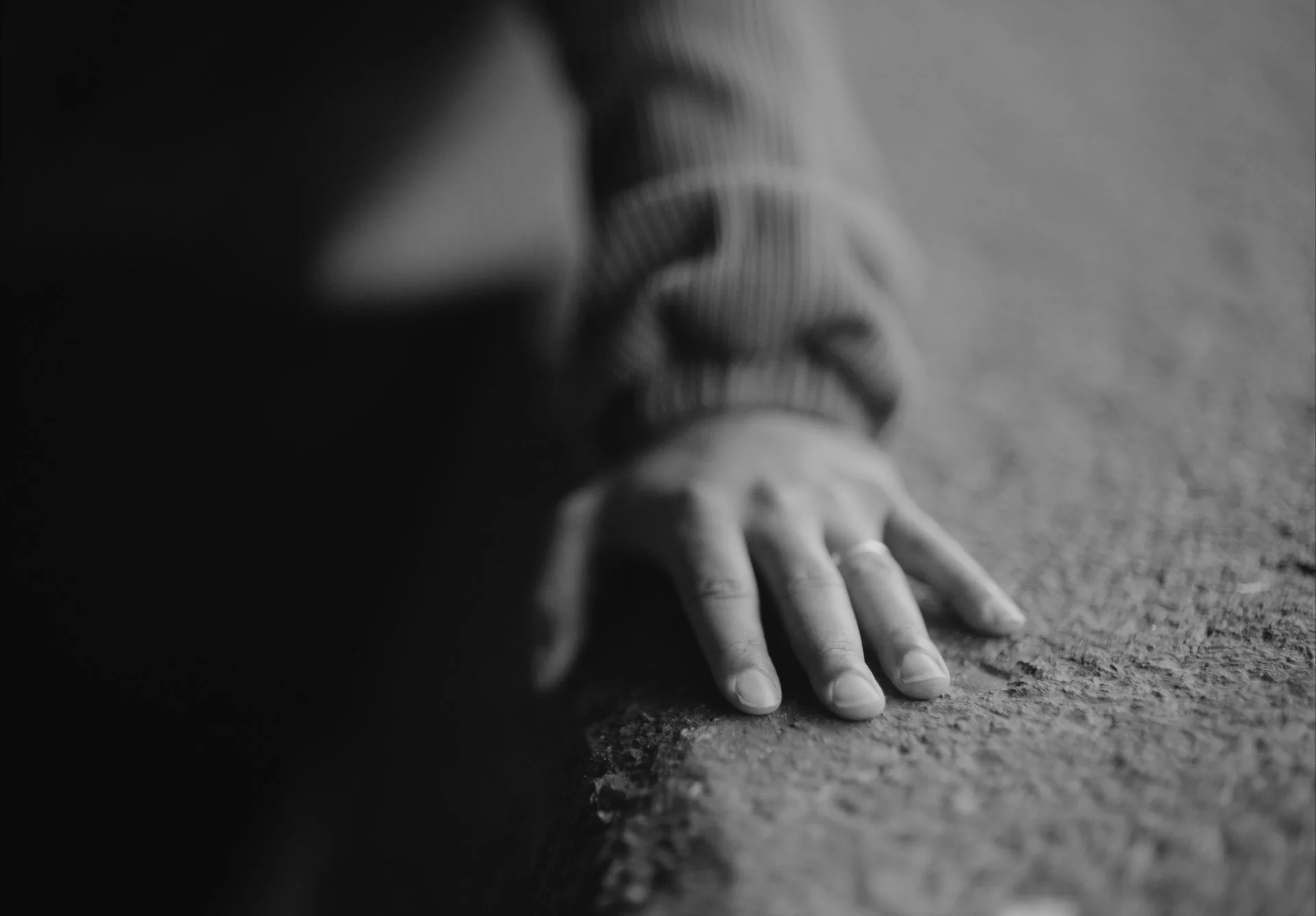 Black and white photo of a person's hand and part of their face resting on a textured surface.