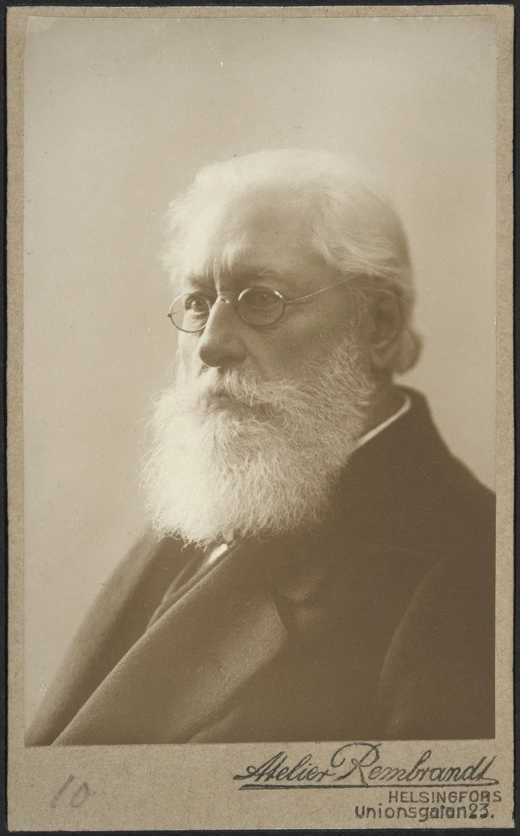 Black and white portrait of an elderly man with white hair, beard, and glasses, dressed in a dark suit, with text underneath that reads 'Alois Rembrahd, Helsingfors, Unionsgatan 23'.
