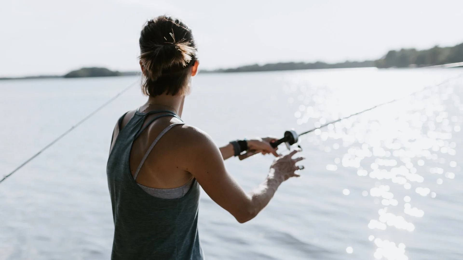 A woman fishing by a body of water on a sunny day.
