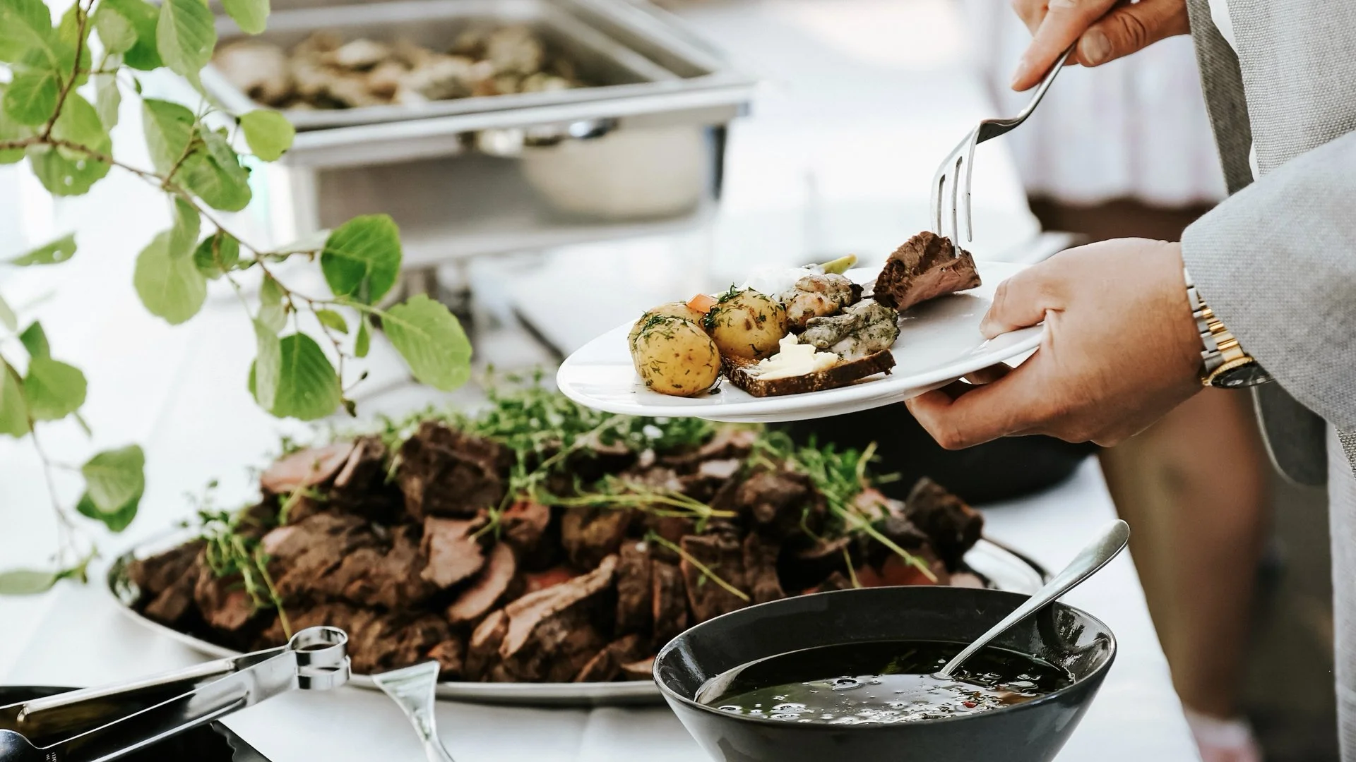 Person serving food from a buffet, including potatoes, meat, and sauce