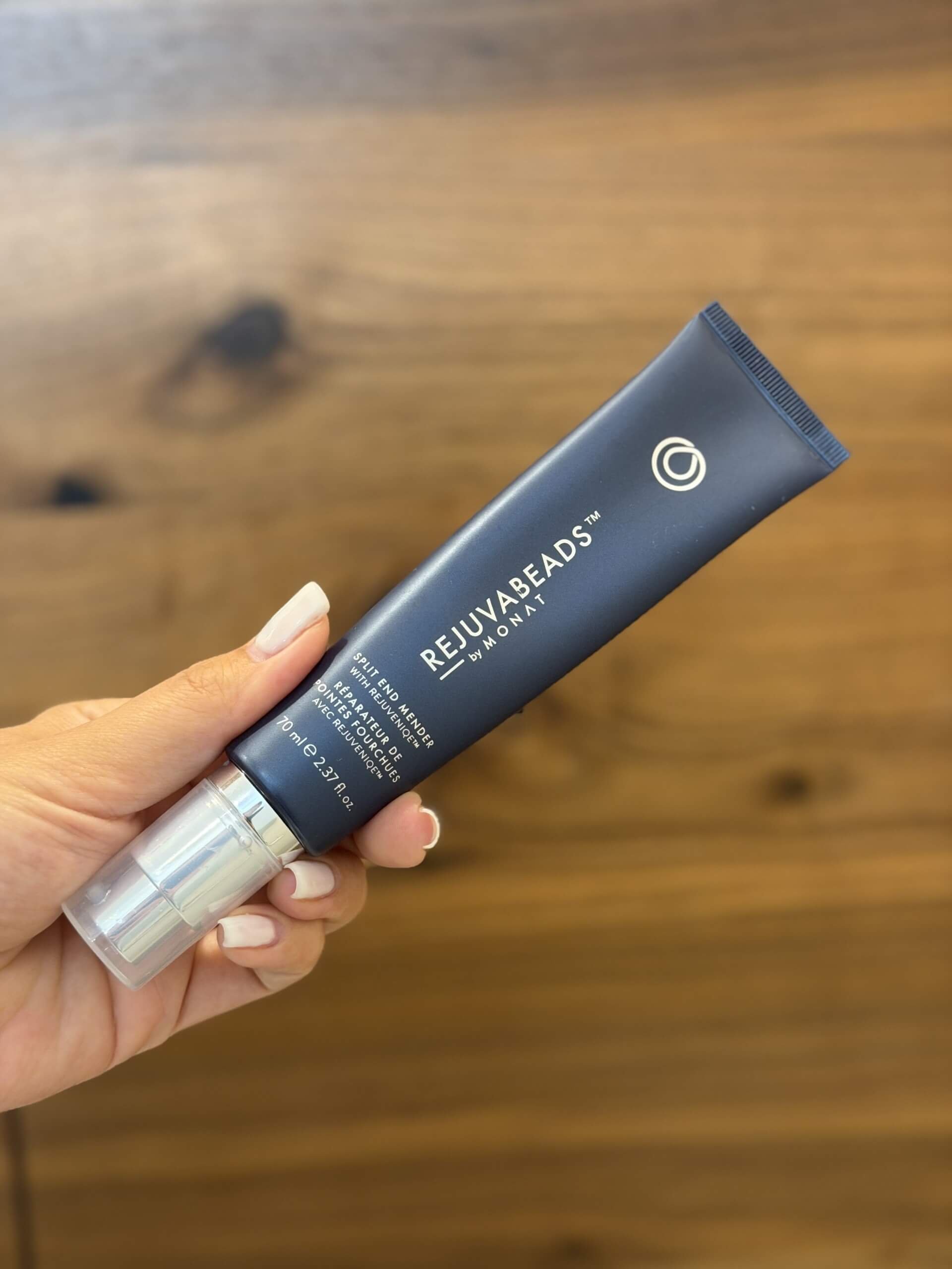 Nahaufnahme einer Hand, die eine Tube RejuvenBeads by MoM Beauty verschönert auf einen Holztisch hält.