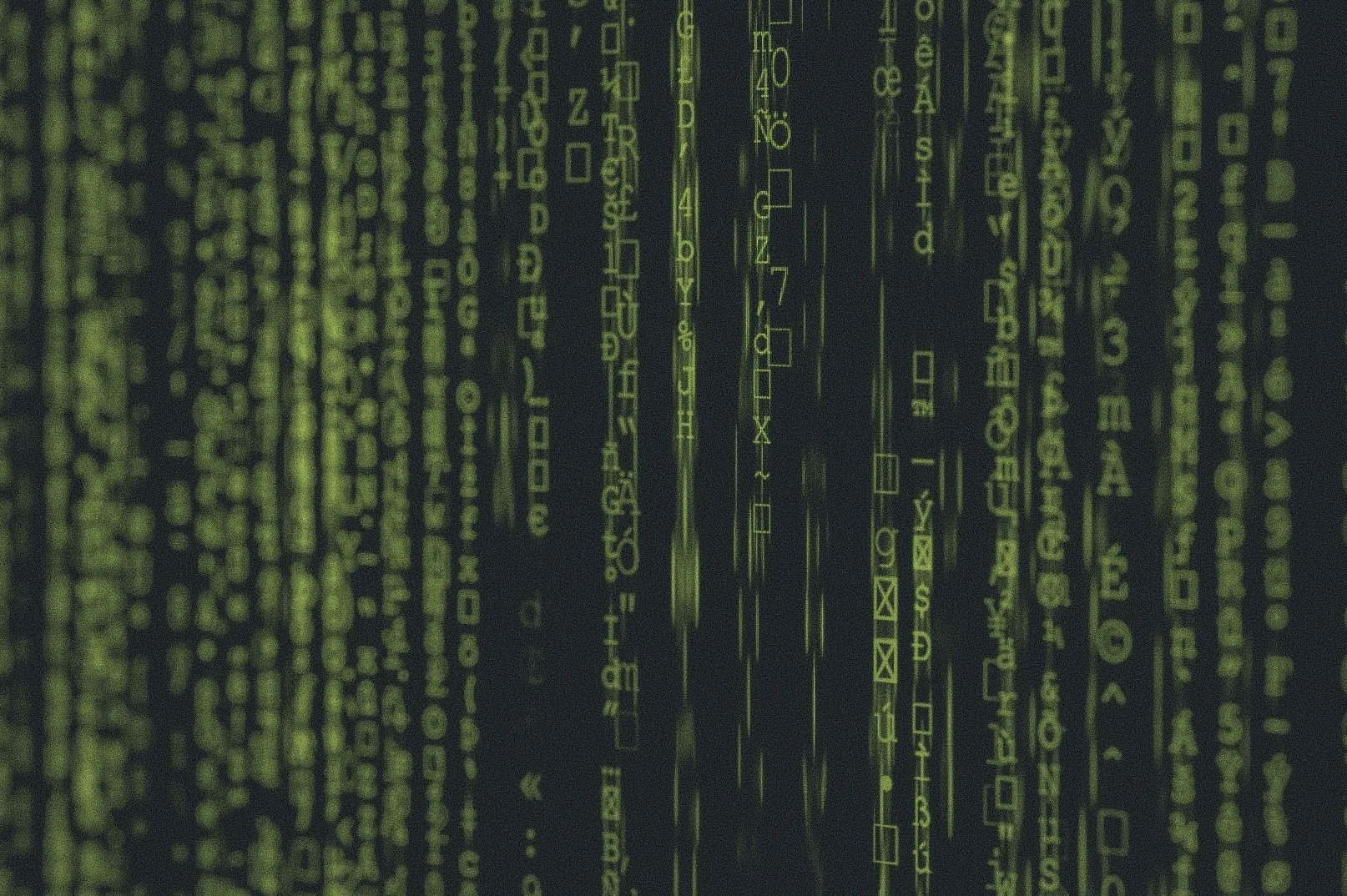 Green computer code and symbols displayed on a dark background, resembling digital or hacking interface.