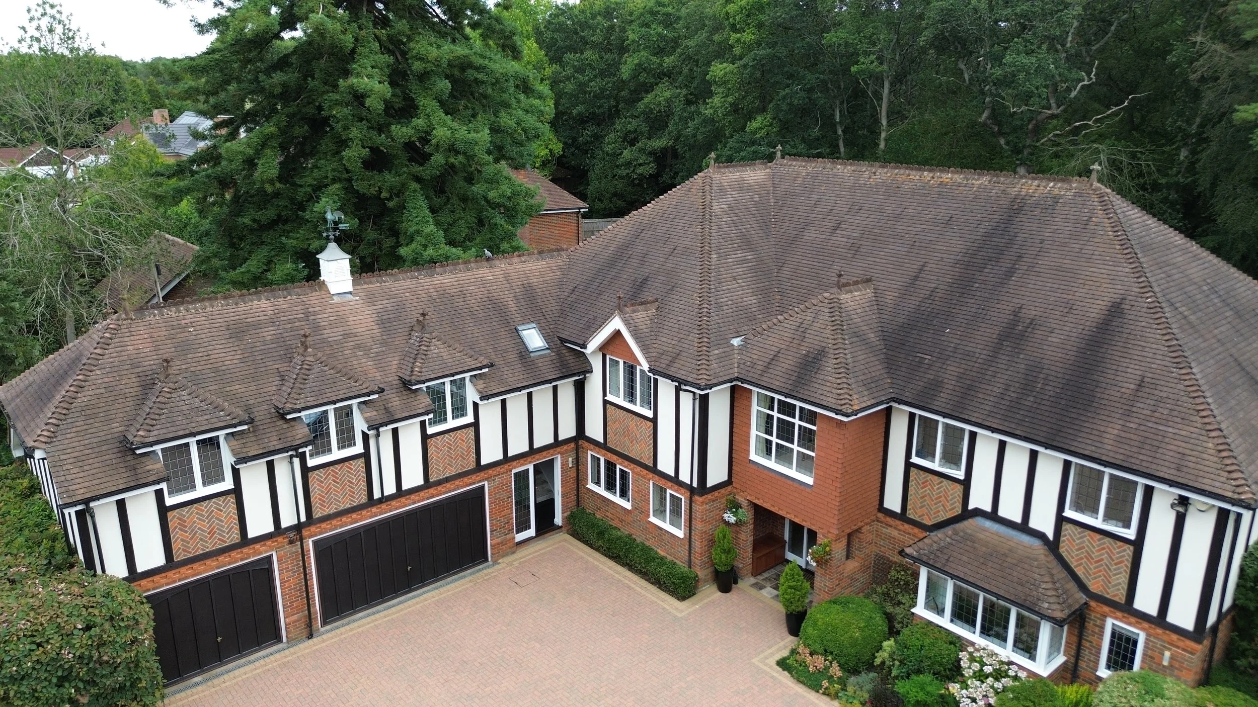 A large house with a tiled roof surrounded by trees, with multiple windows and a driveway in front.