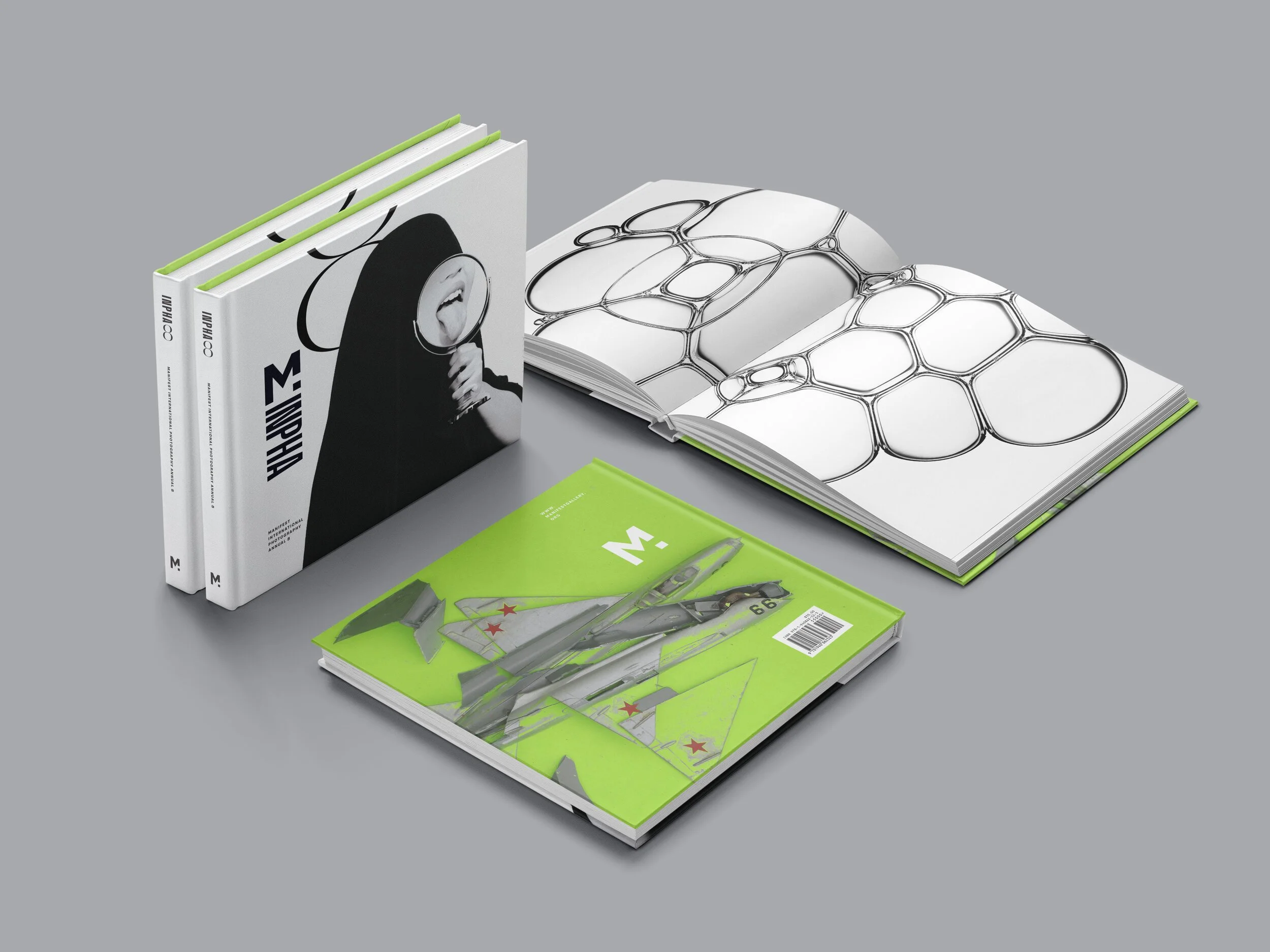 Collection of art books and magazines on a gray surface, including two black-and-white covers, an open blank book with black abstract line art, and a green magazine with model aircraft images.