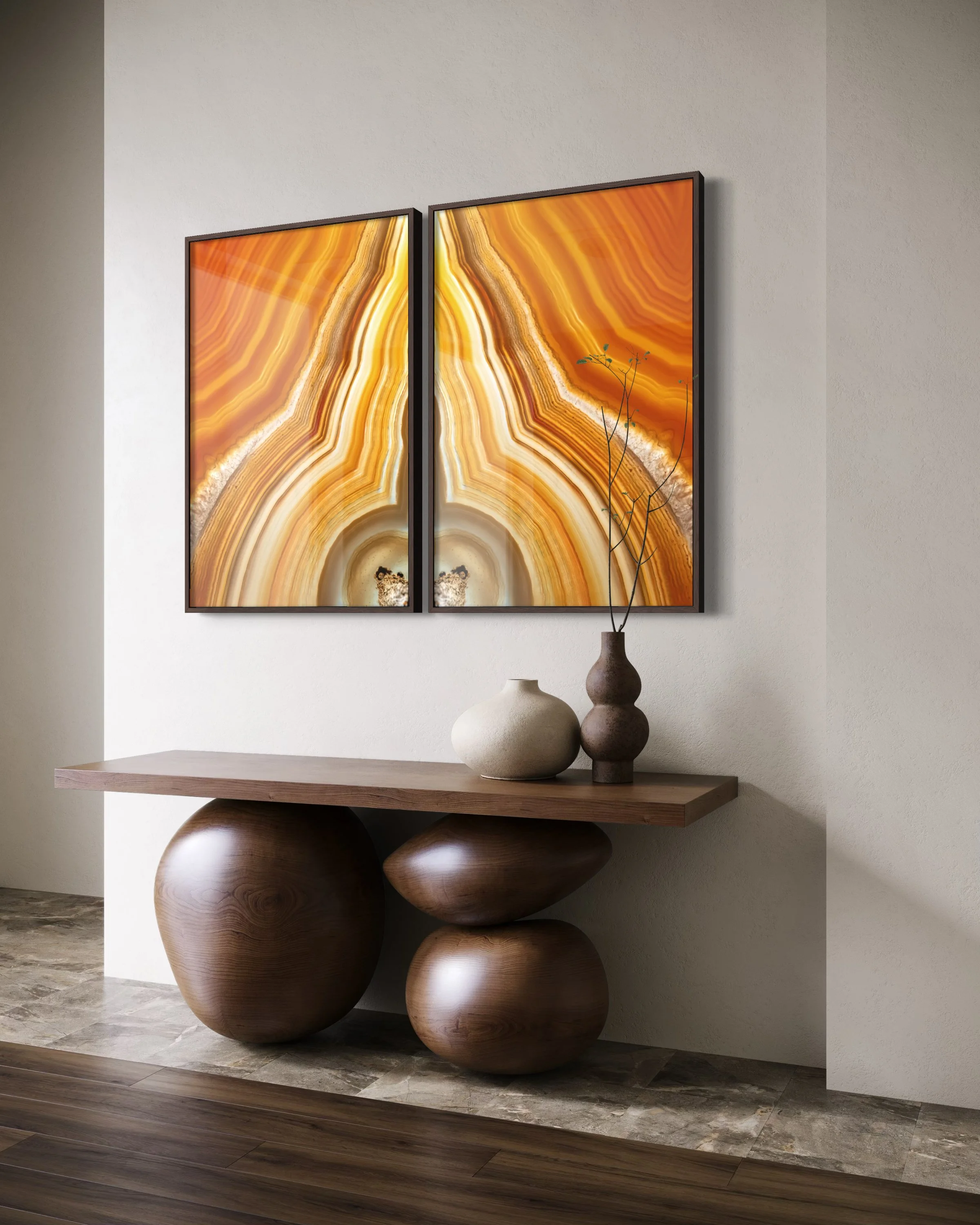 Duas telas decorativas com padrão de onça em tons de laranja e amarelo acima de uma mesa de madeira, decorada com três vasos de diferentes tamanhos e cores, na parede de fundo branca.