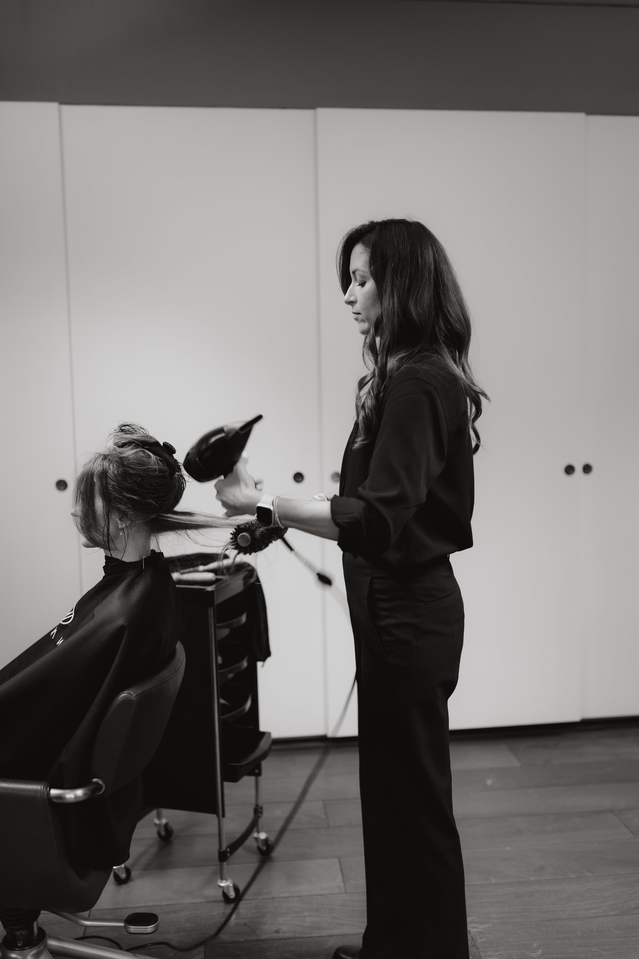 Schwarz-Weiß-Foto einer Friseurin beim Föhnen eines Kunden im Schönheitssalon.