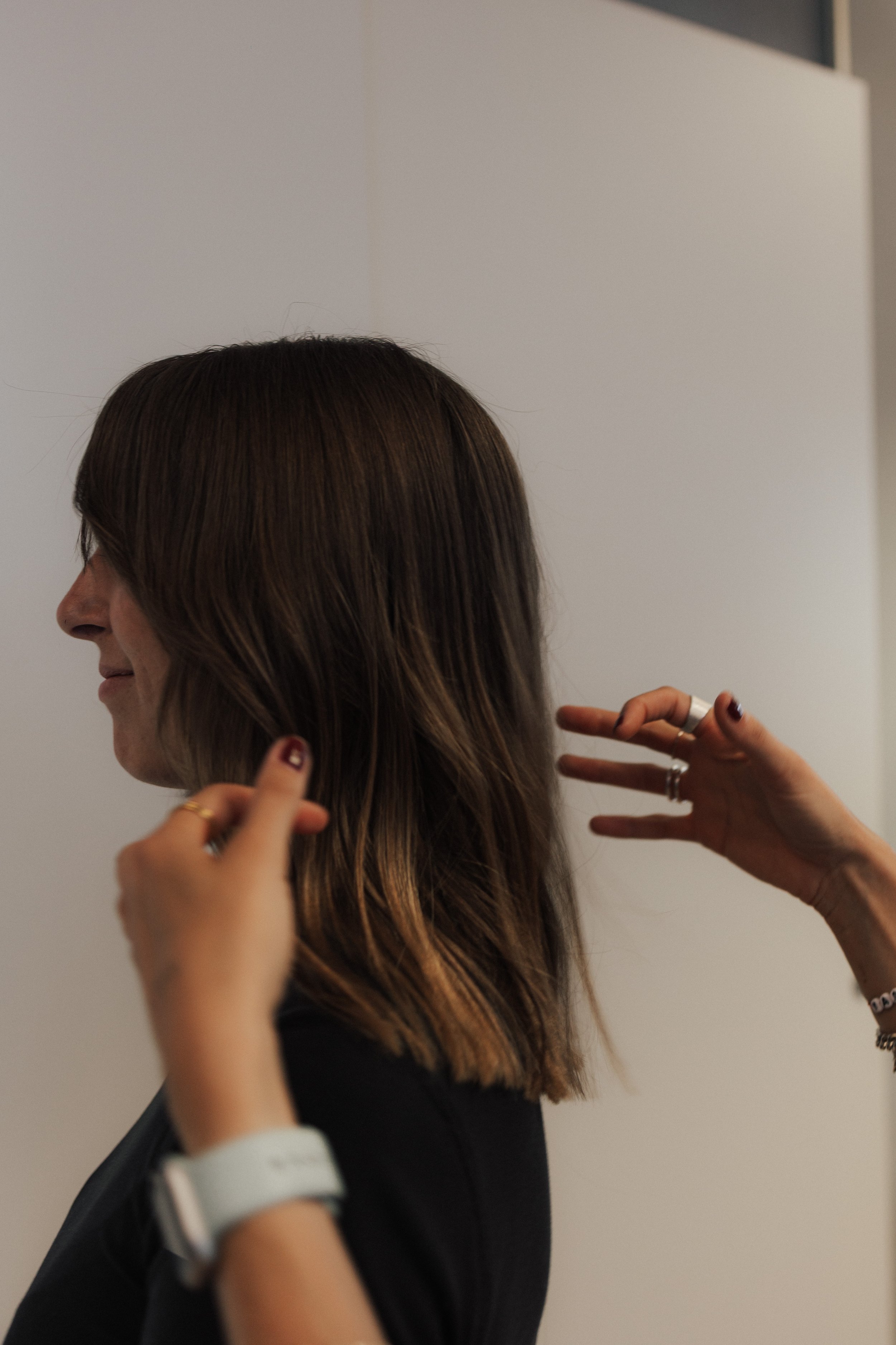 Eine Frau mit braunen, glatten Haaren, die von einer Person gestylt wird, während sie stehen, vor einem weißen Hintergrund.