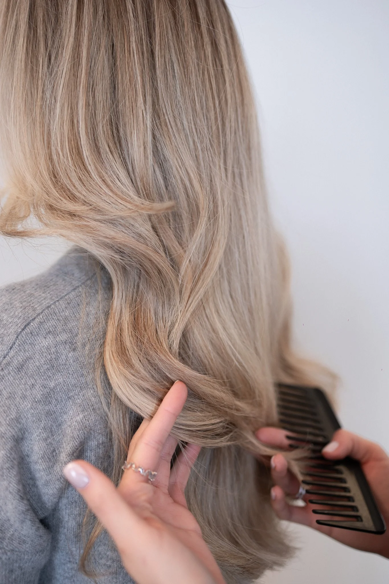 Nahaufnahme einer Frau mit langen, gewellten, blonden Haaren, die mit einem Kamm gestylt werden.