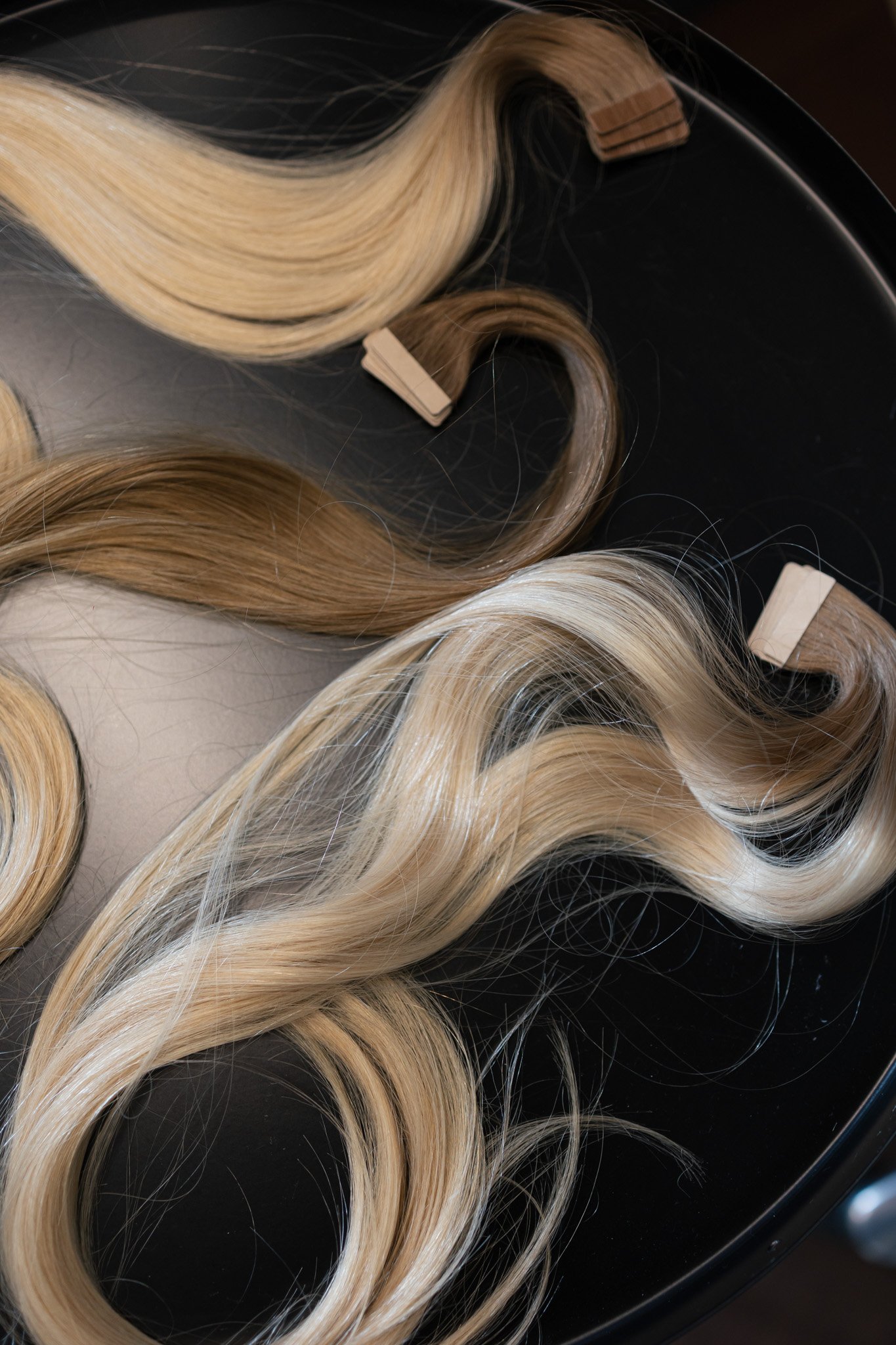 Verschiedene Lockenwindeln für Haarverlängerungen in verschiedenen Blondtönen auf schwarzem Hintergrund.