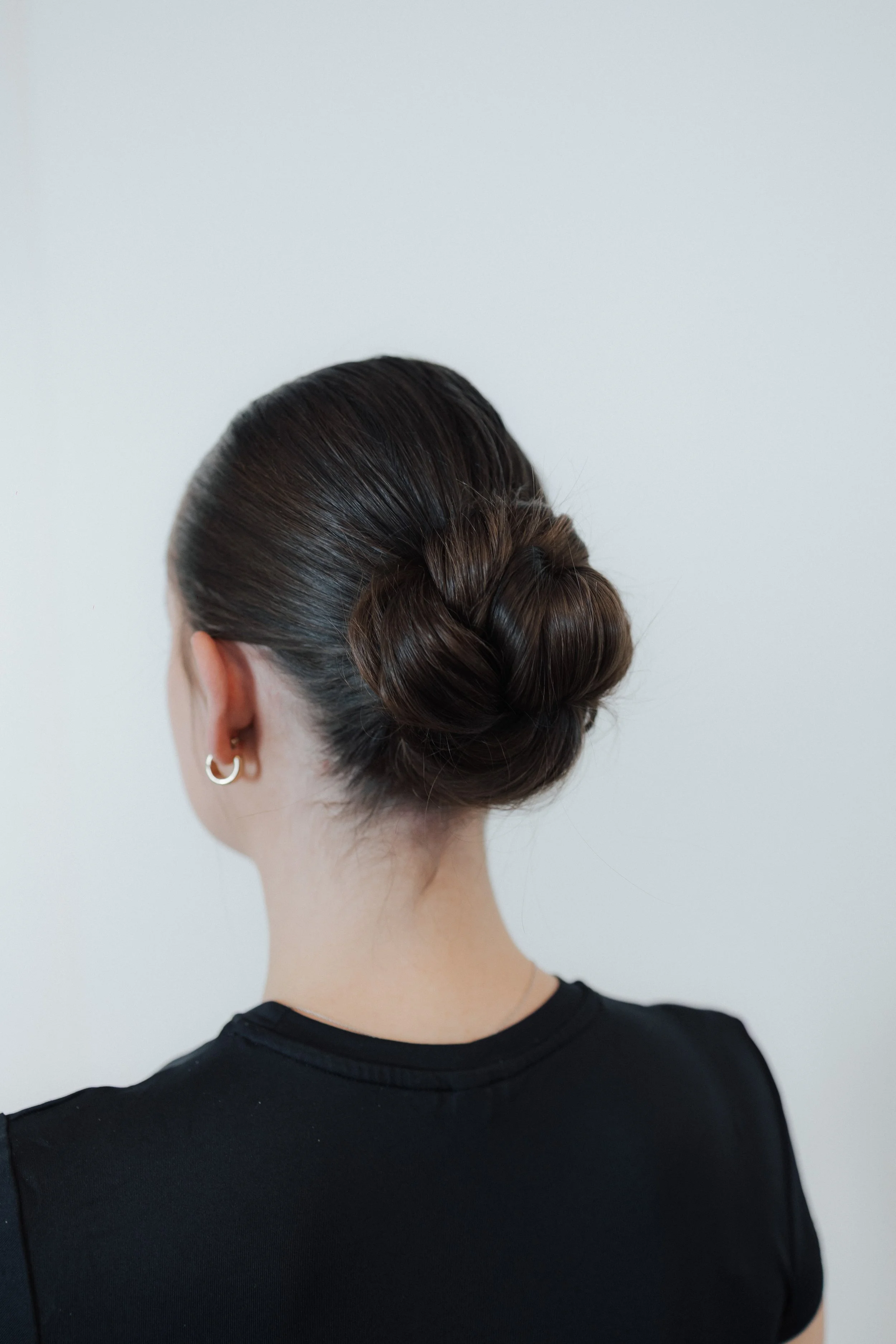 Dunkle, glänzende Haare, die zu einem französischen Zopf geflochten sind, getragen von einer Frau, deren Rücken sichtbar ist, vor weißer Wand.
