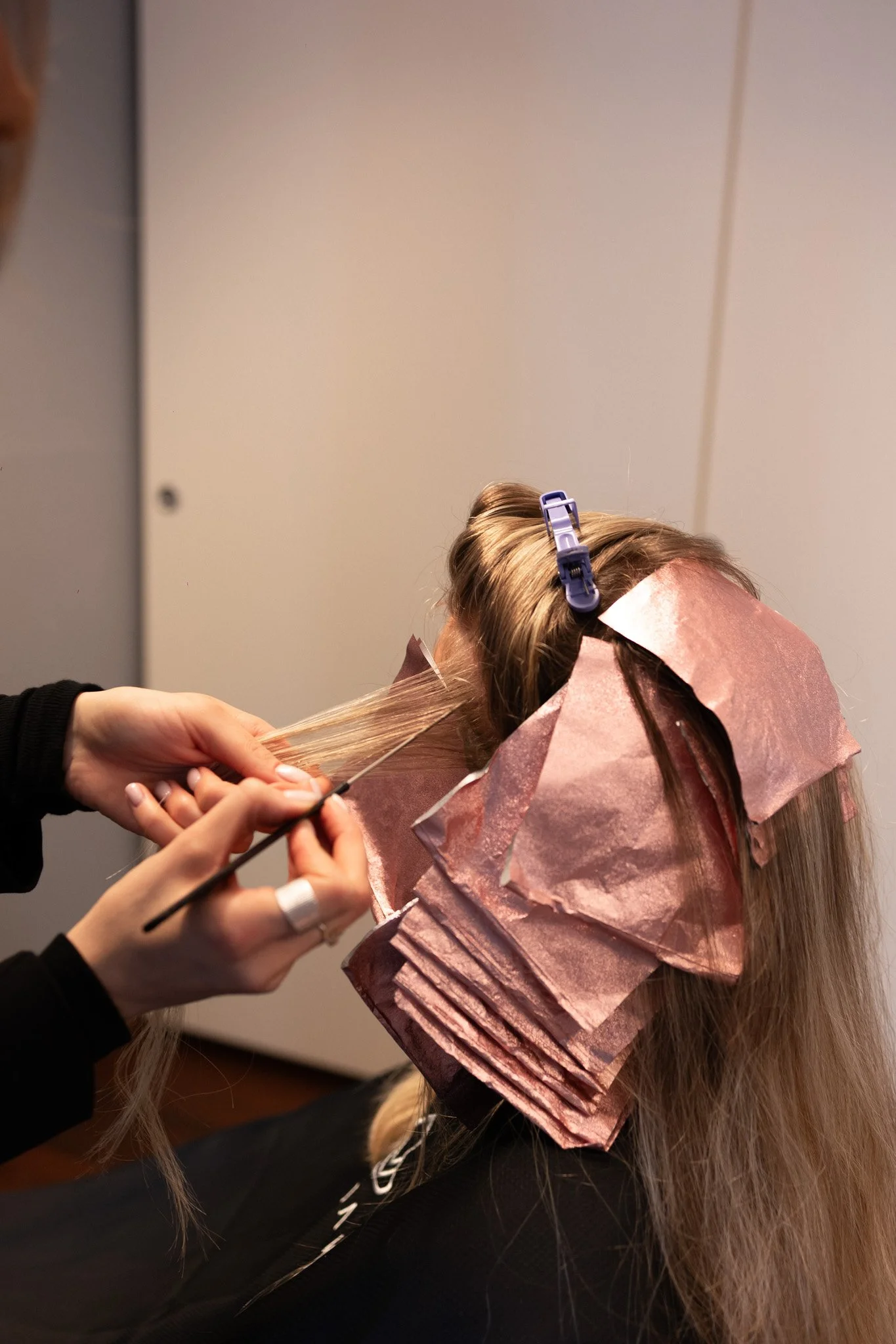 Frau erhält eine Haarfärbung im Salon, mit Alufolie im Haar und Friseurin, die Pinsel benutzt.