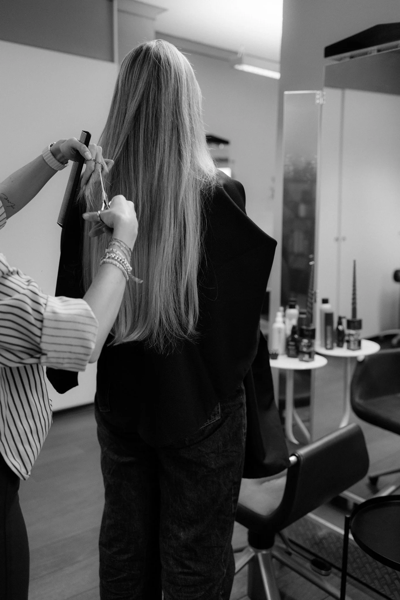 Schwarz-Weiß-Foto einer Friseurin, die eine Frau mit langen blonden Haaren schneidet, in einem Friseursalon.