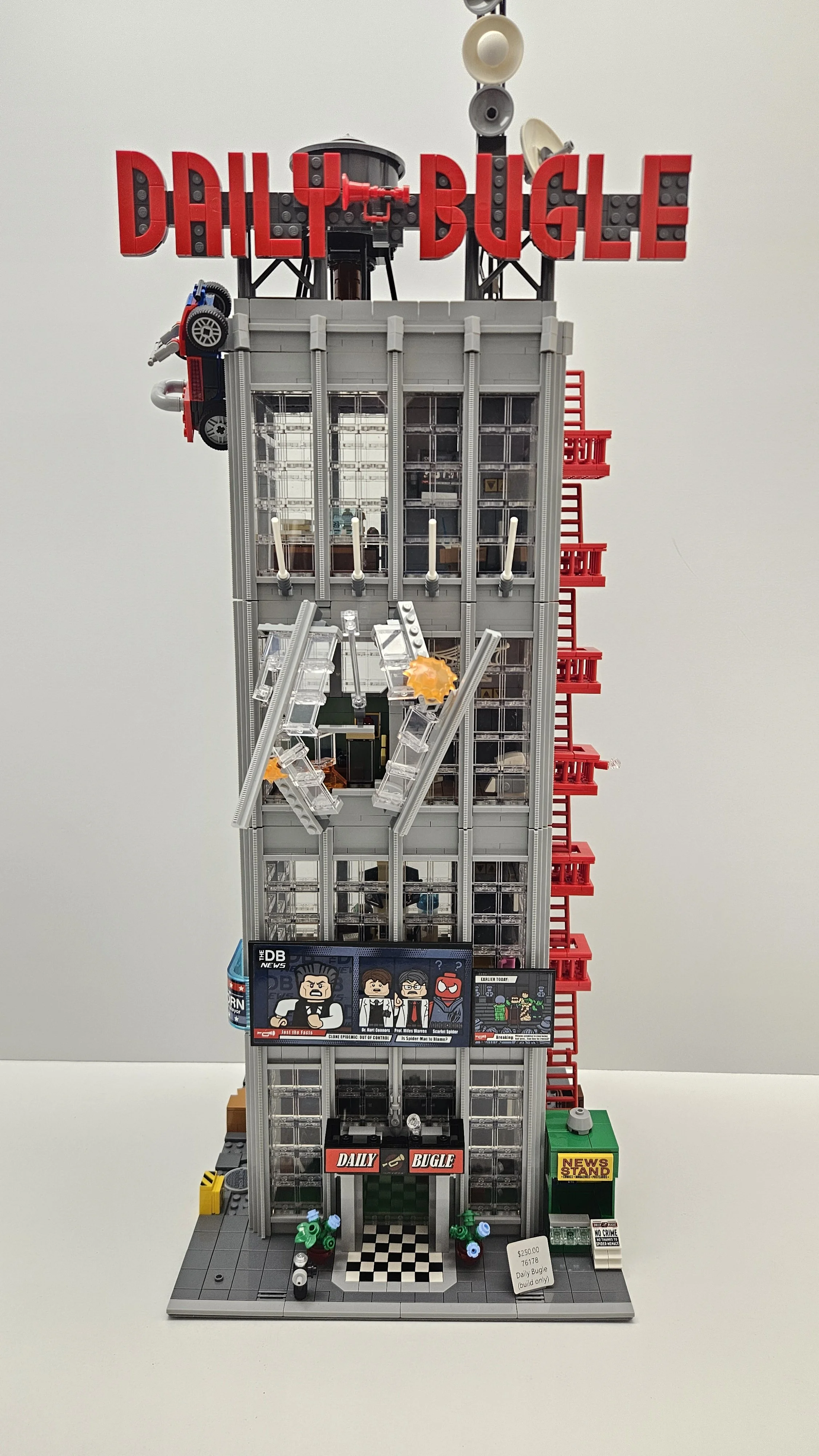 A detailed Lego replica of a news building with a red "DAILY BUGLE" sign on top, featuring multiple floors, windows, a red fire escape, and a newspaper stand outside. The building has animated elements like explosions and figures simulating a news scene.