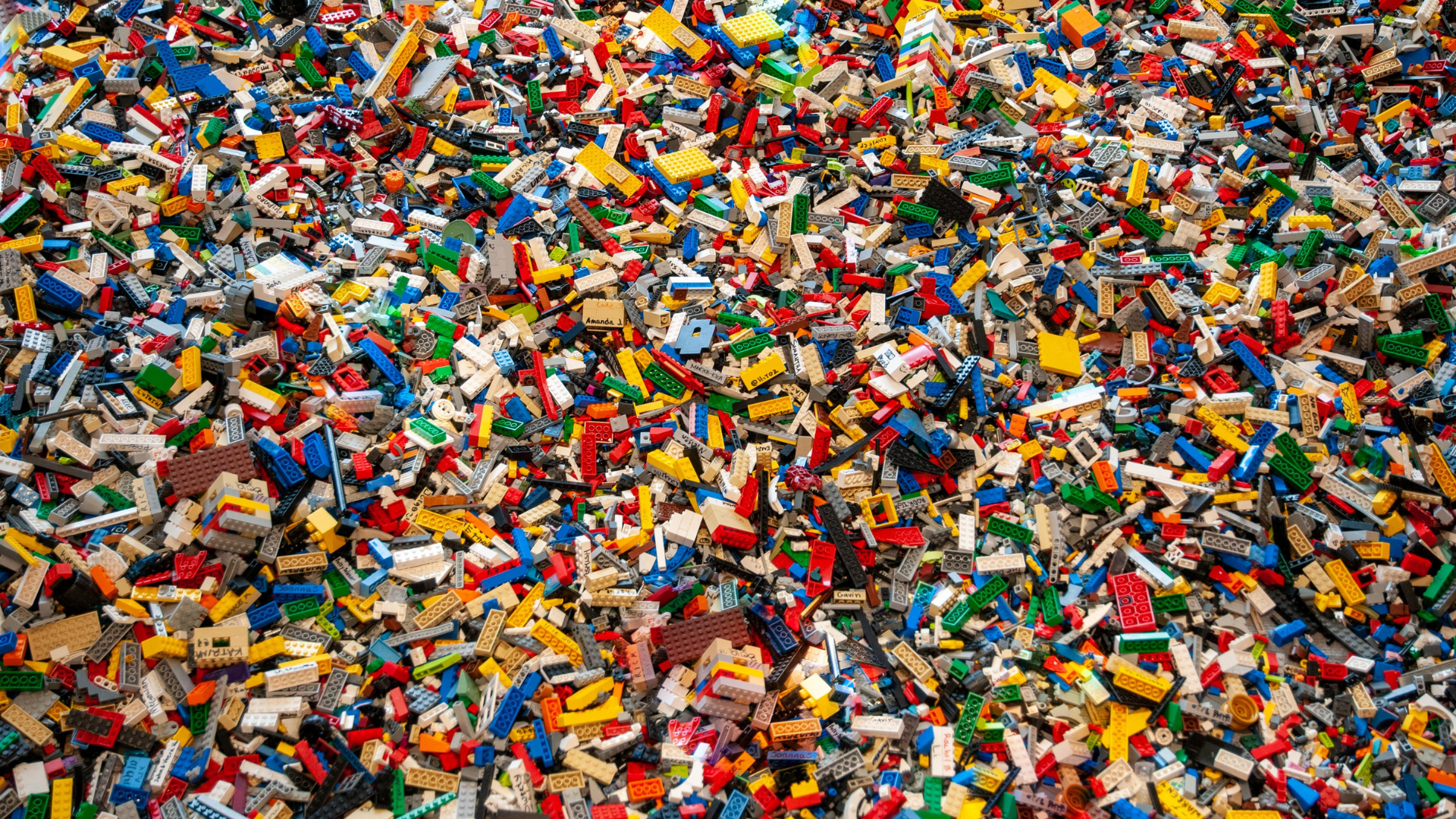 A large pile of assorted small plastic building blocks and LEGO bricks, mostly in primary colors like red, blue, yellow, green, along with some black, white, and gray pieces.