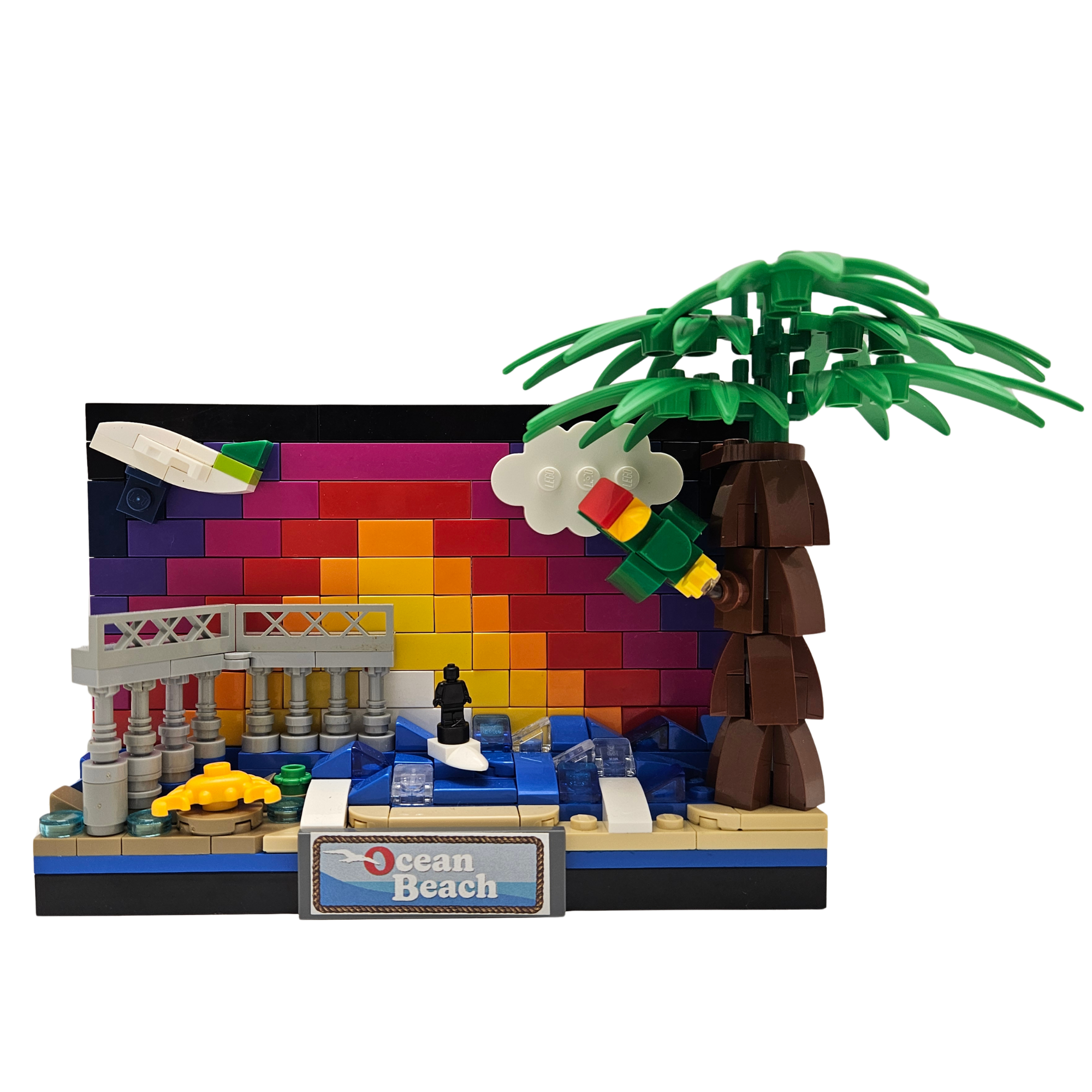 Colorful LEGO beach scene with umbrella, palm tree, waves, and a small figure, with a sign reading 'Ocean Beach'