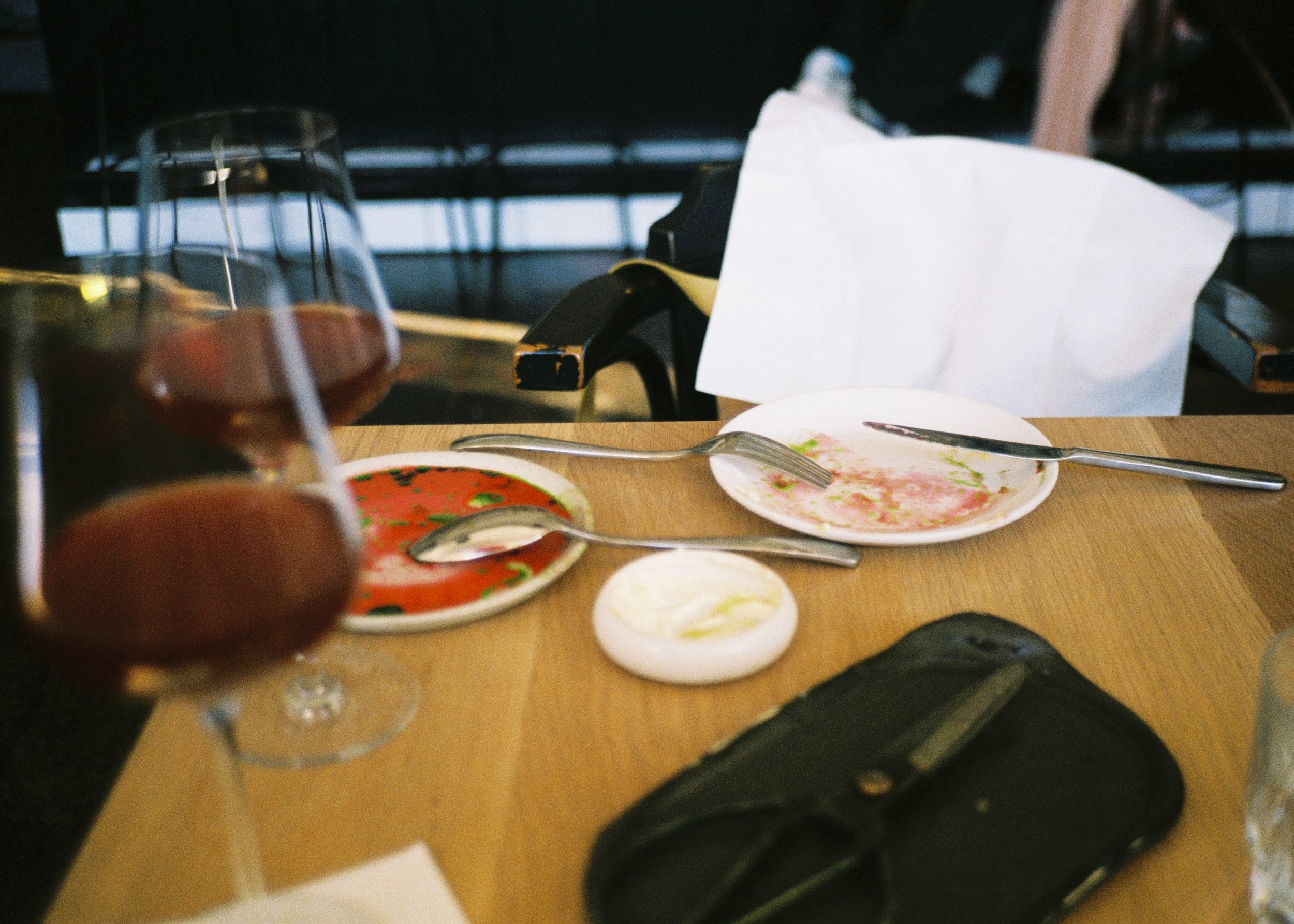 Partially eaten plates of food, two glasses of red wine, a knife, and a fork on a wooden table in a restaurant setting.