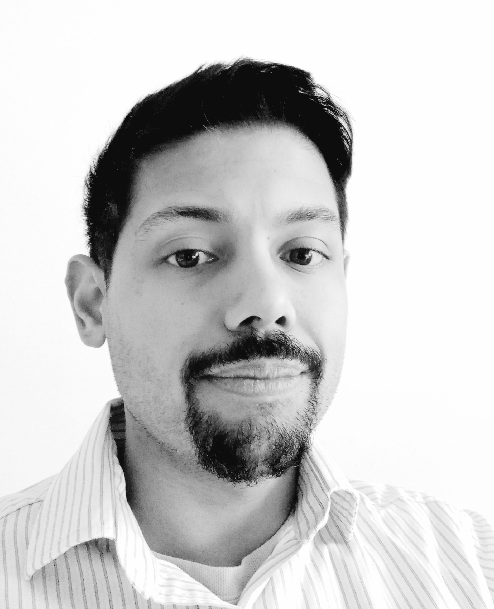 Close-up black and white photo of a man with short dark hair, facial hair, wearing a collared striped shirt.