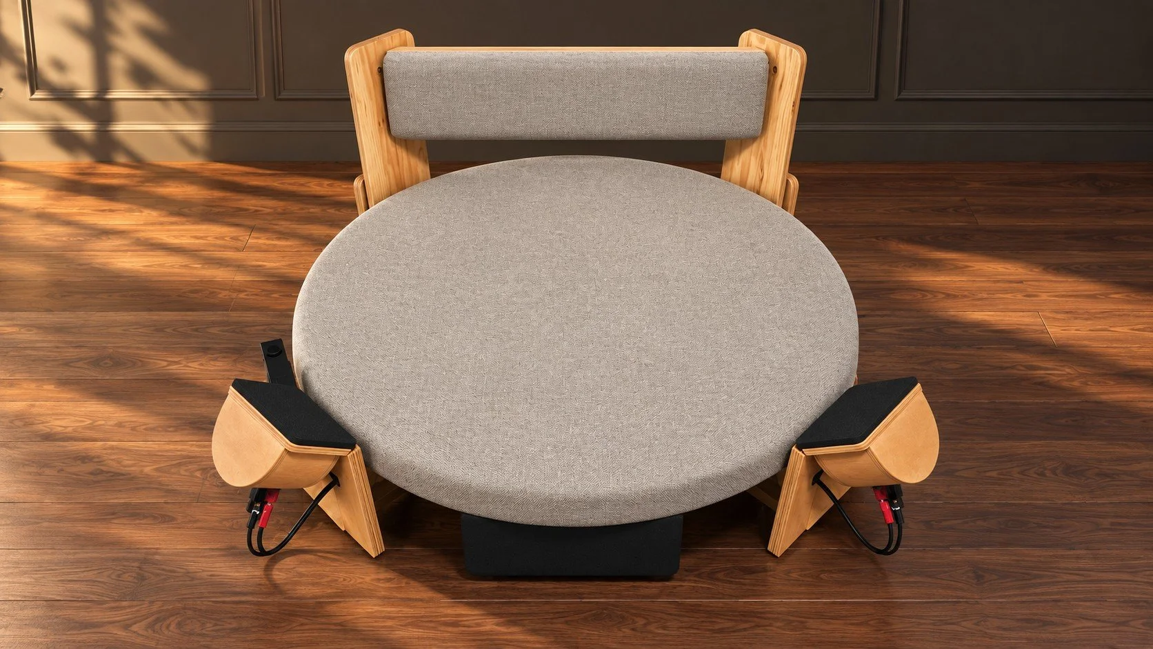 A round table with a grey surface in a room with wooden flooring and dark paneled walls, accompanied by a wooden chair with a grey upholstered backrest.