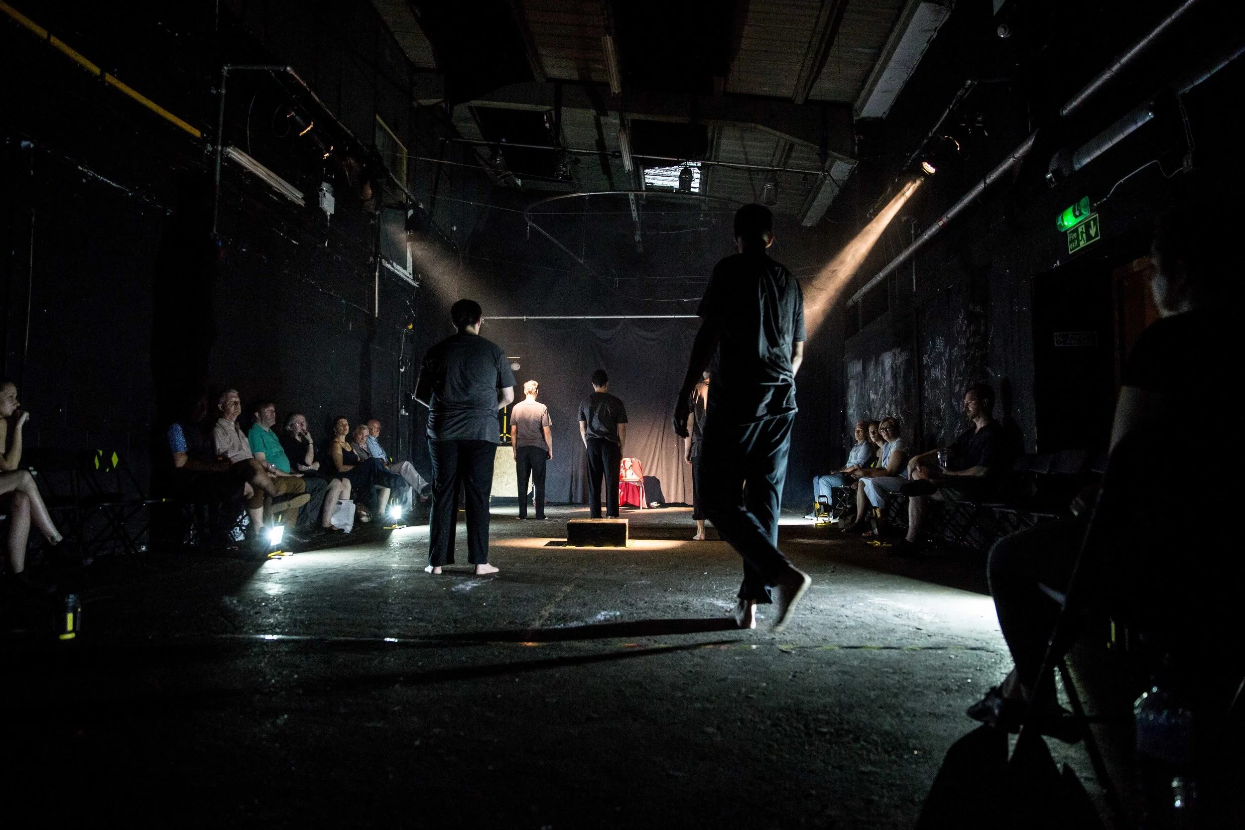 People on a stage performing in front of an audience in a dimly lit venue with a spotlight on the performers.