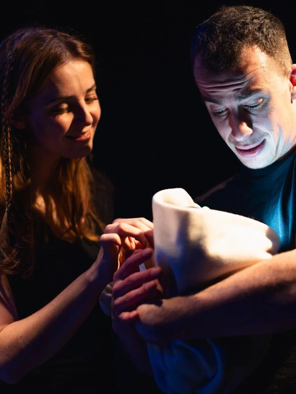 A man and a woman looking at a piece of fabric or cloth together in a dark room, illuminated by a blue light.