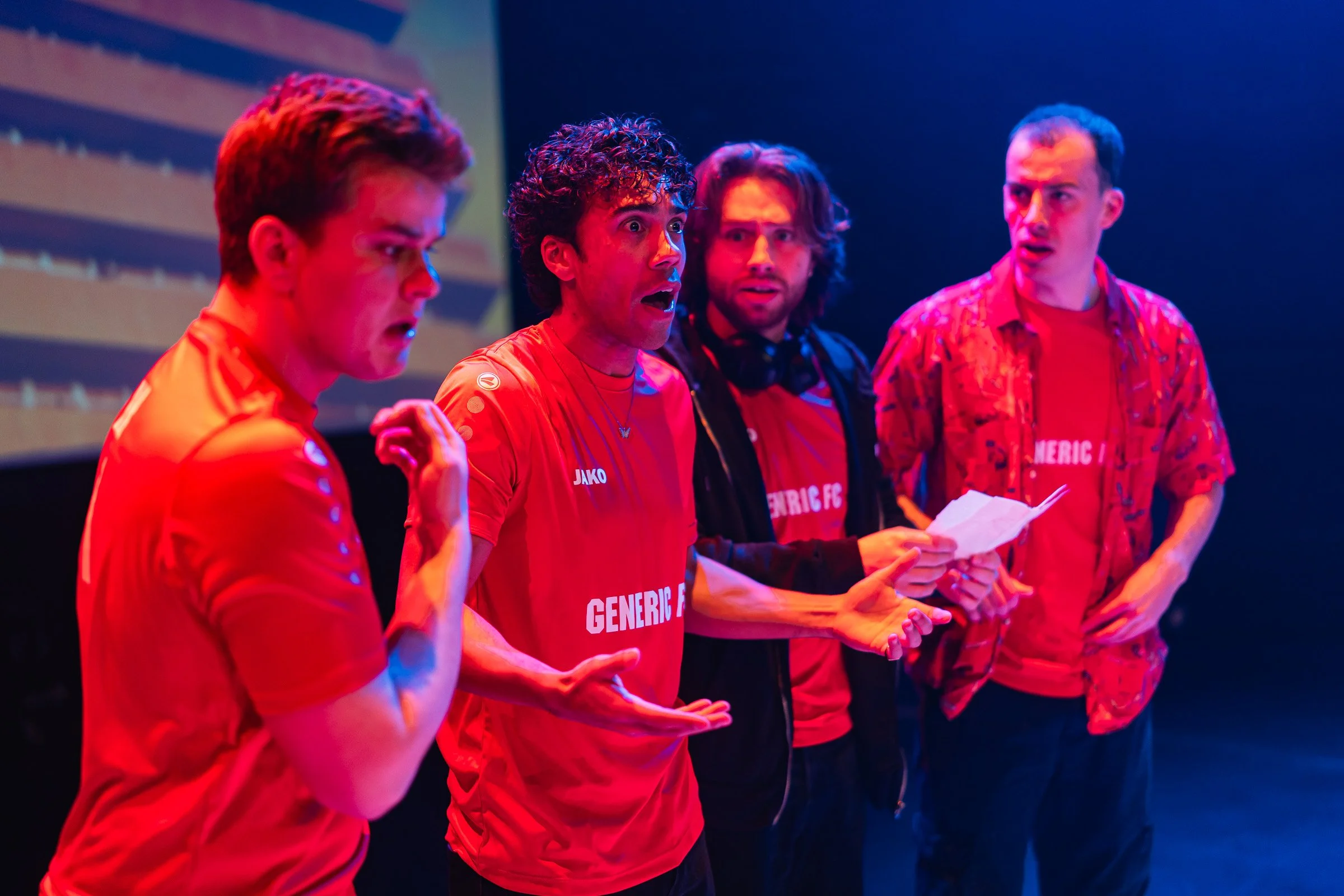 Four men in red shirts standing in a row, appearing surprised or focused, with a colorful background.