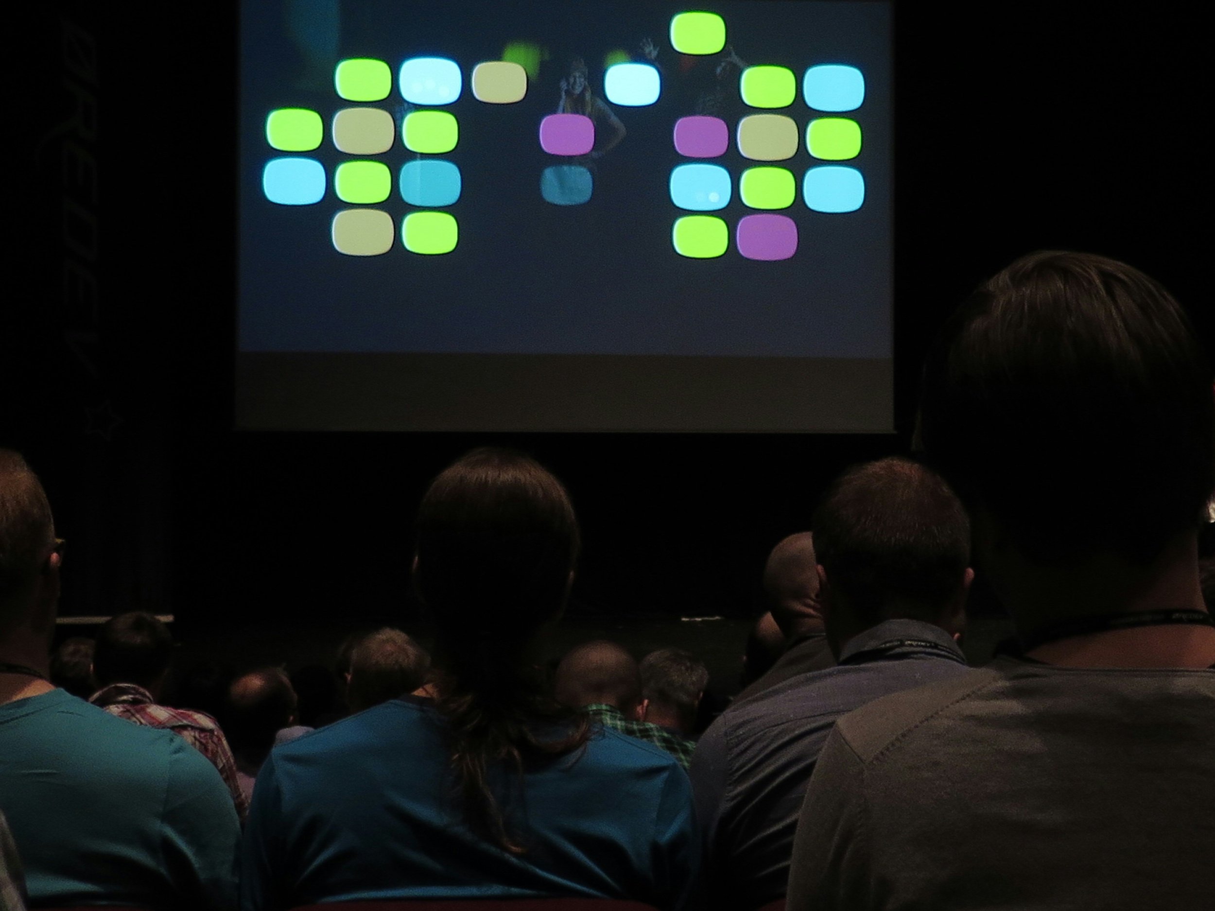 Concert audience watching a large screen displaying colorful squares and a performer.