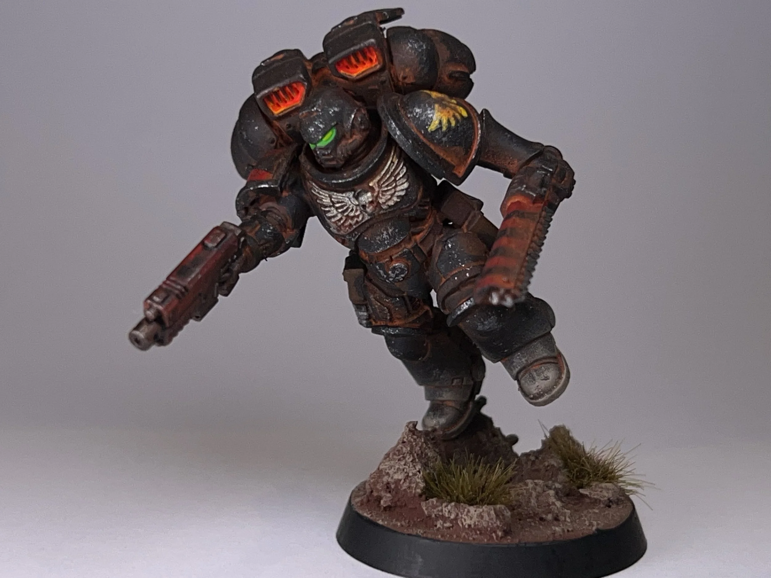 A detailed miniature figure of a WWII soldier in black and industrial orange armor, wielding a rifle, standing on a textured base with grassy terrain.