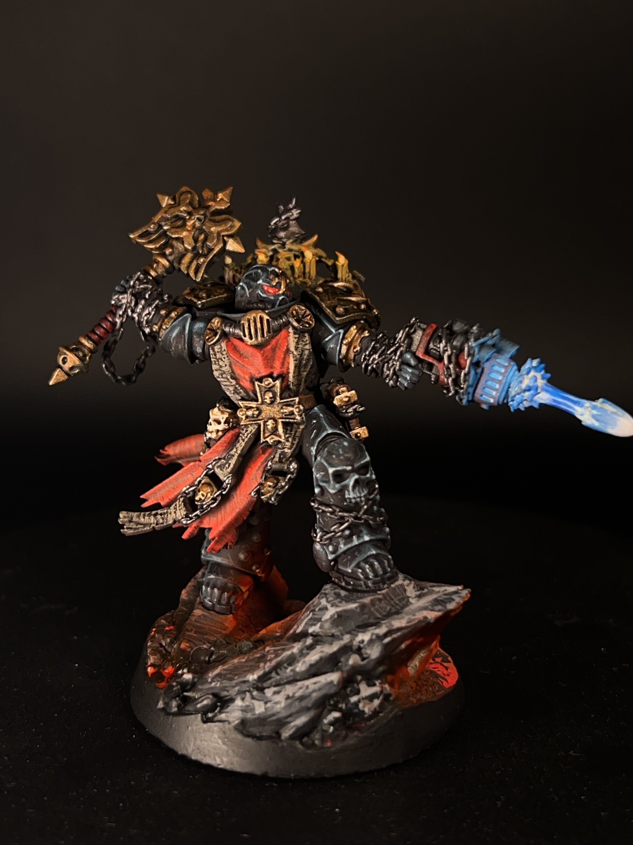 A detailed painted miniature figure of a warrior in black armor with gold and red accents, wielding a glowing blue weapon, standing on a decorative rocky base against a black background.
