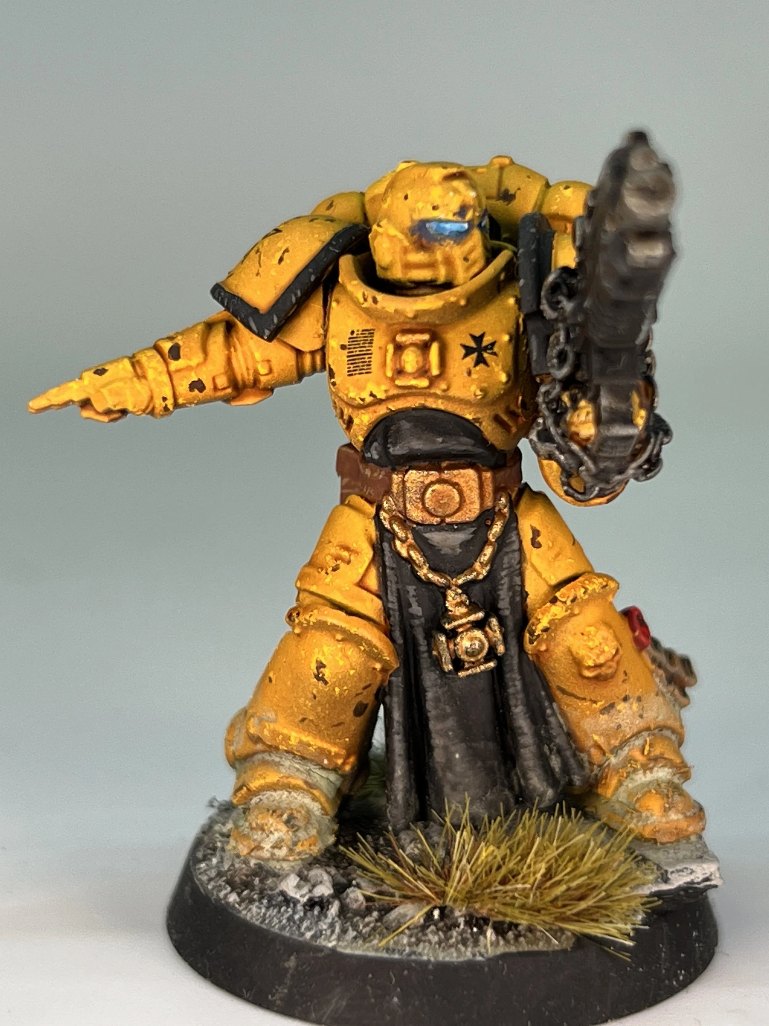 A painted miniature figure of a sci-fi soldier in yellow armor holding a large gun, standing on a rocky base with grass details.