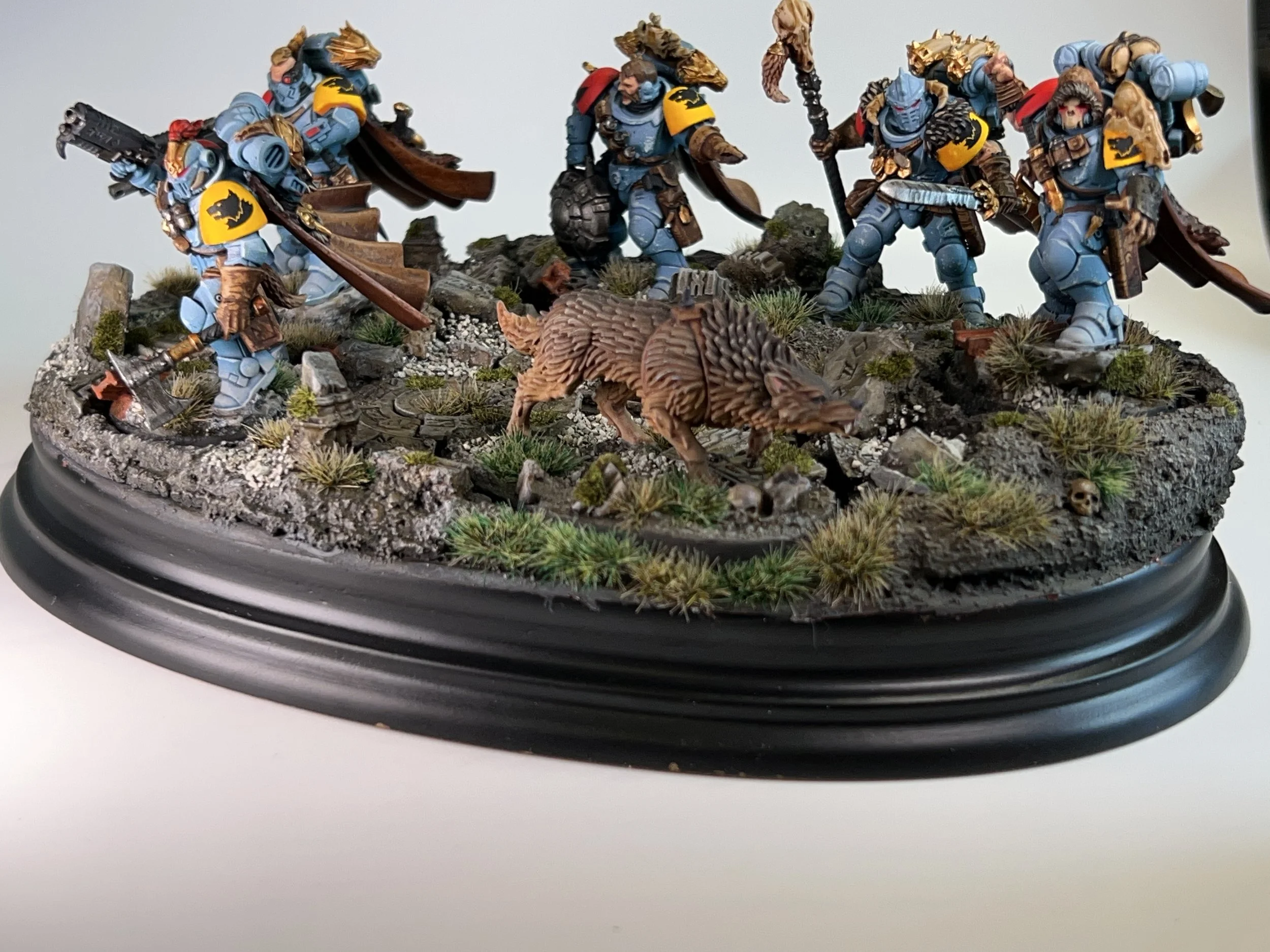 Miniature tabletop figurines of armored soldiers with wolf pelts and shields, posing on a rocky terrain with grass and skull details, on a black circular base.