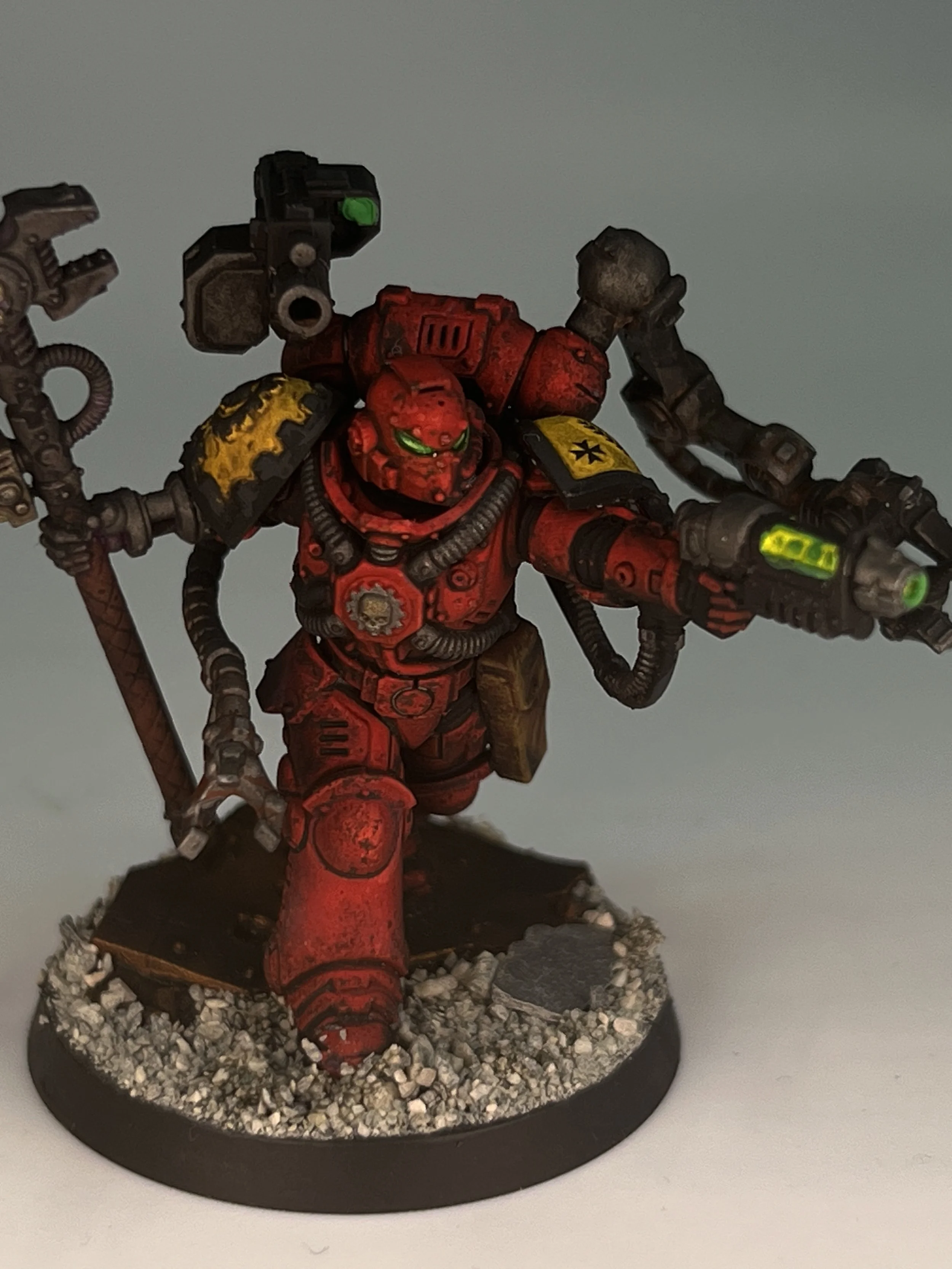 Miniature red armored soldier with green eyes, wielding weapons, standing on rocky terrain base.
