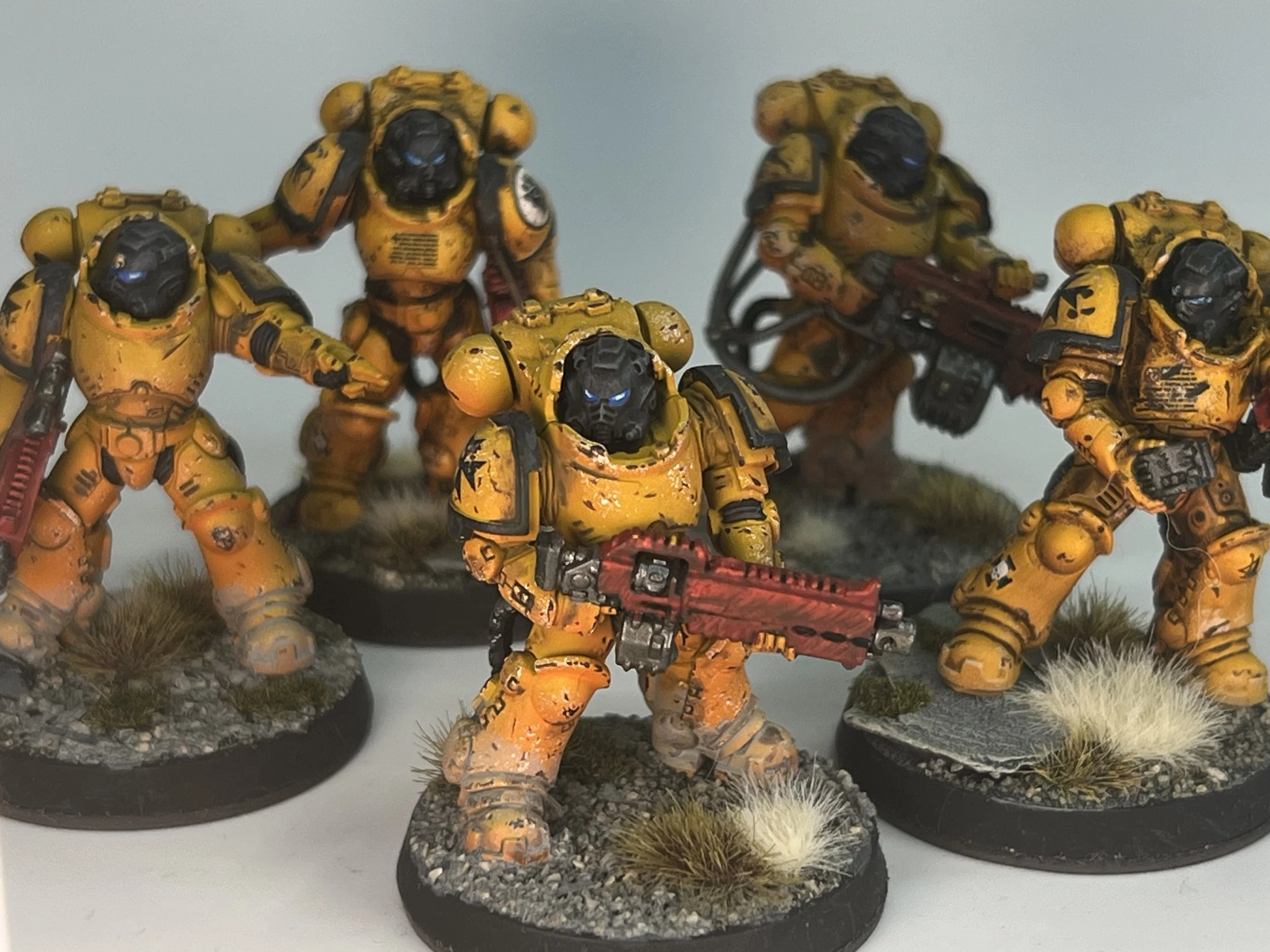 A group of yellow-armored futuristic soldiers with black visors and various weapons, posed on round bases decorated with grass and rocky terrain.