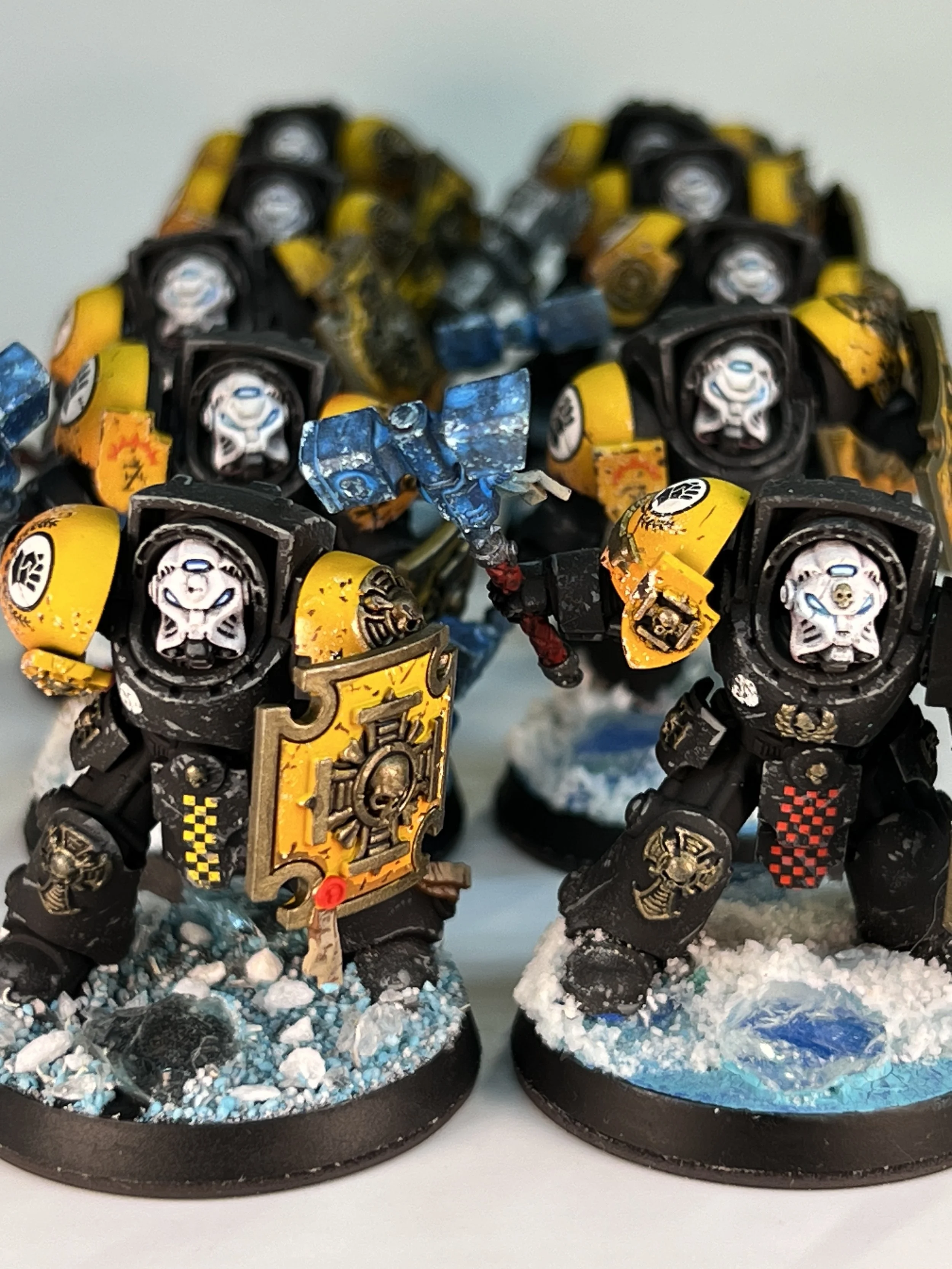 Miniature figurines of armored soldiers, painted yellow and black, on snowy bases with blue and white terrain details.
