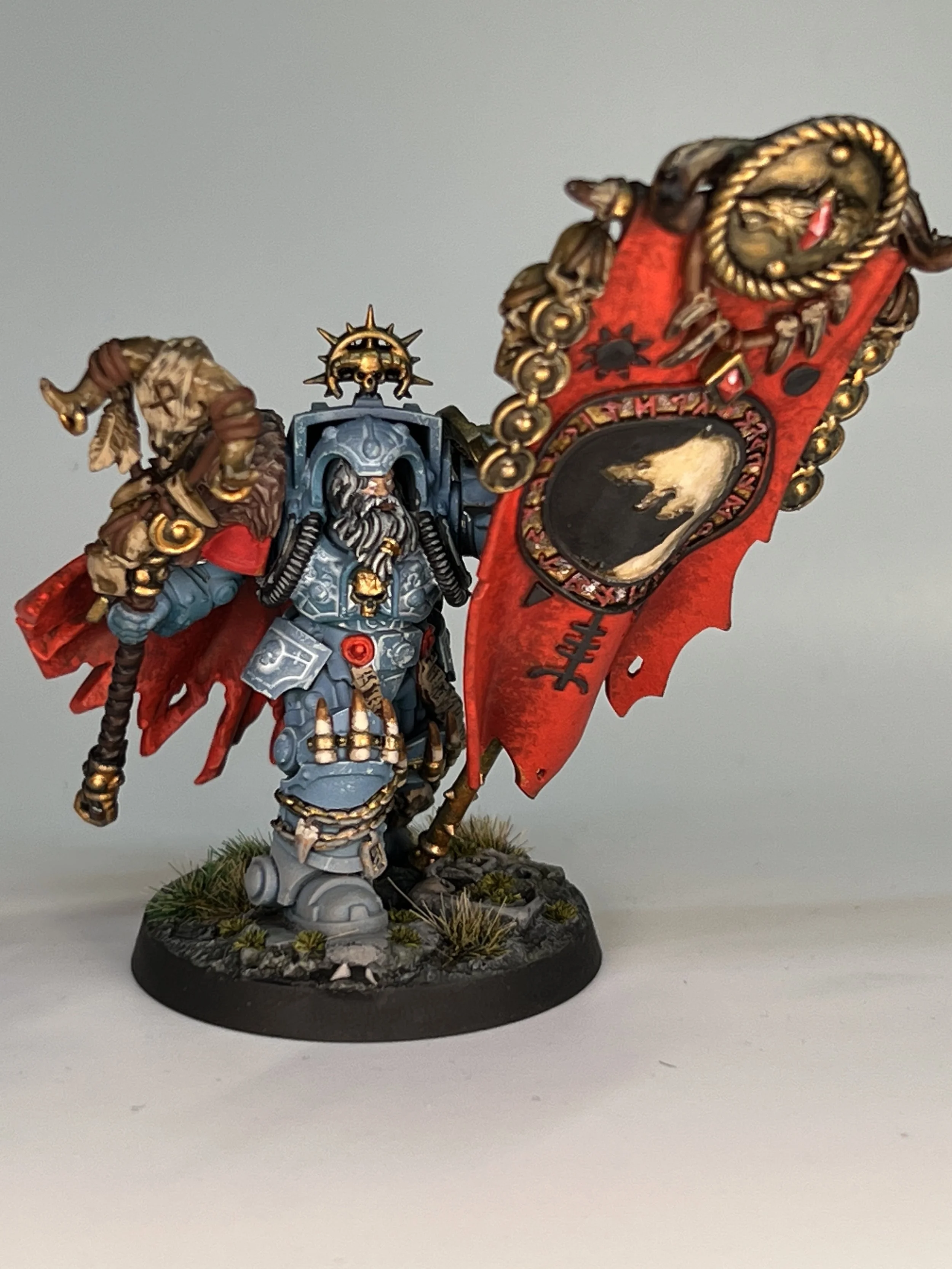 A detailed miniature figurine of a fantasy warrior riding a red bannered creature, holding a staff, standing on a round base with grass and rocks.