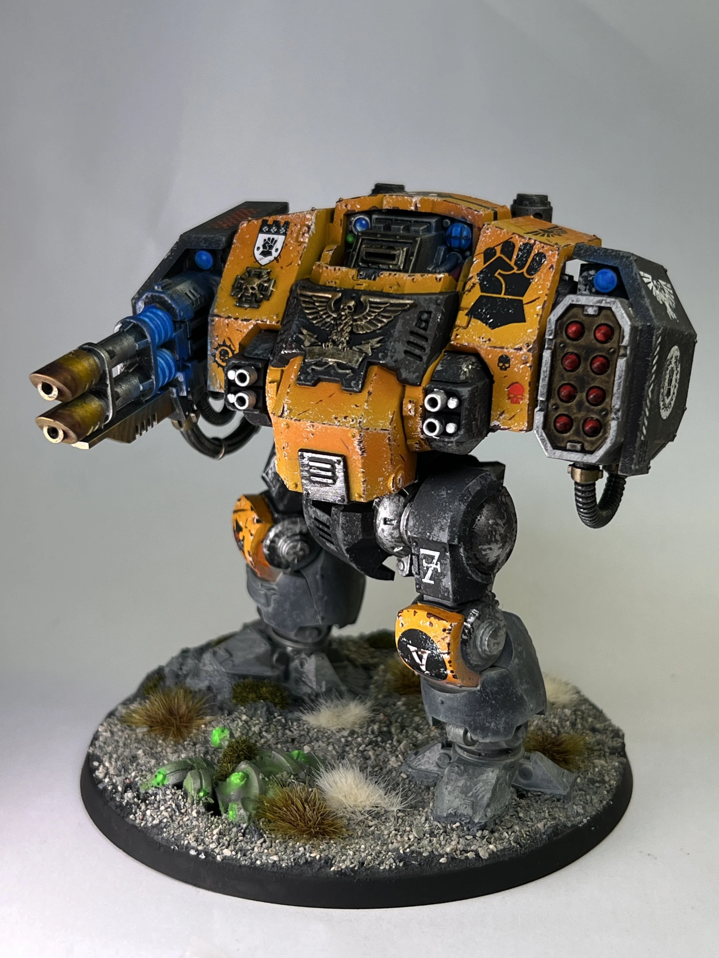Painted miniature model of a sci-fi robot standing on a detailed base with grass, rocks, and green glowing elements.