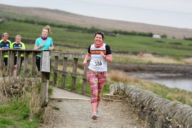 A woman running on a trail with a group of people behind her during a race, in a rural outdoor setting.