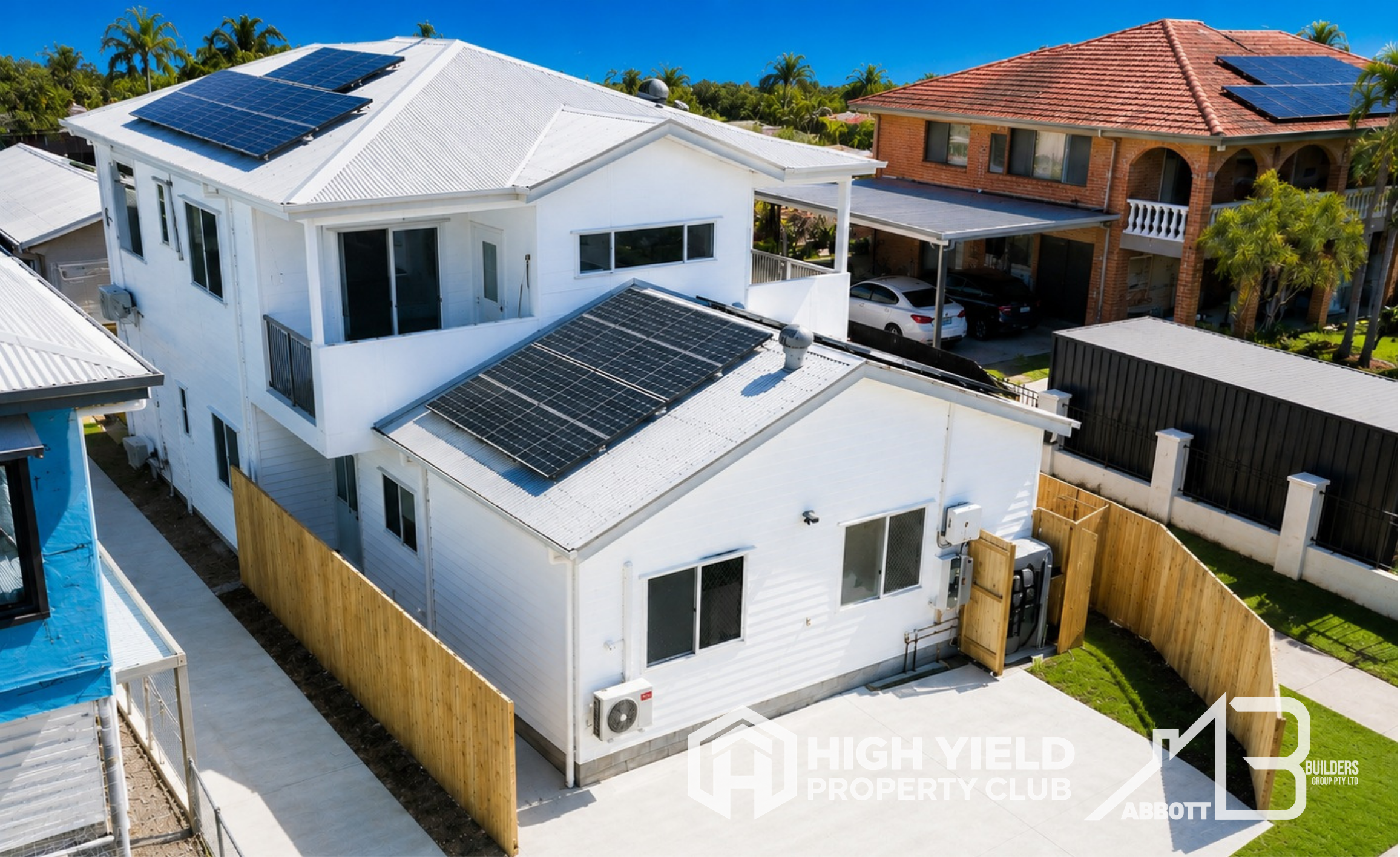A rooming accomodation house. Aerial view of residential houses with solar panels on the roofs, palm trees, and a clear blue sky.