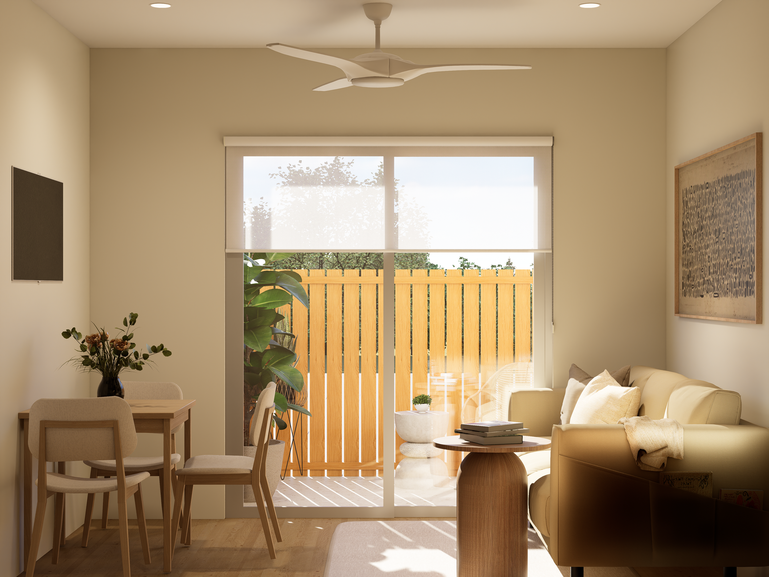 Bright living room with large window and sliding door opening to an outdoor patio with a wooden fence. Interior features include a beige sofa with pillows, a round wooden coffee table with books, a TV on the left wall, a dining table with four chairs, plants near the window, and framed wall art. Ceiling fan and recessed ceiling lights are visible.