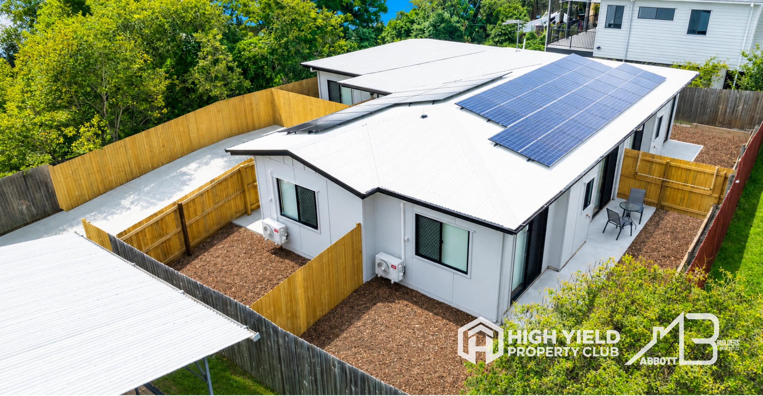 A rooming accomodation house. Aerial view of a modern house with solar panels on the roof, surrounded by a wooden fence and green trees.