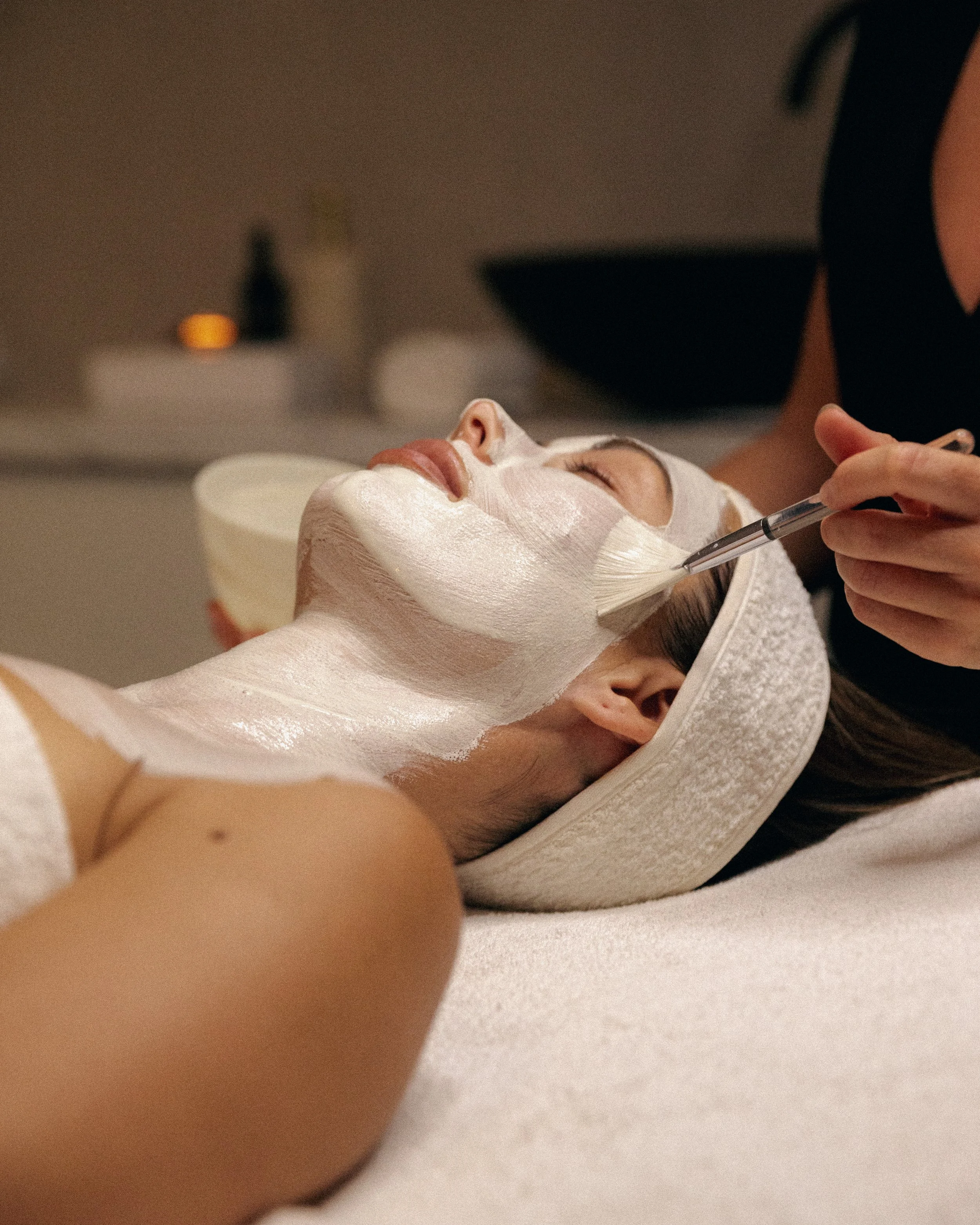 Person receiving a hair wash, lying back with a towel over their face, a hand holding an orange hairbrush, and water flowing from a sink.