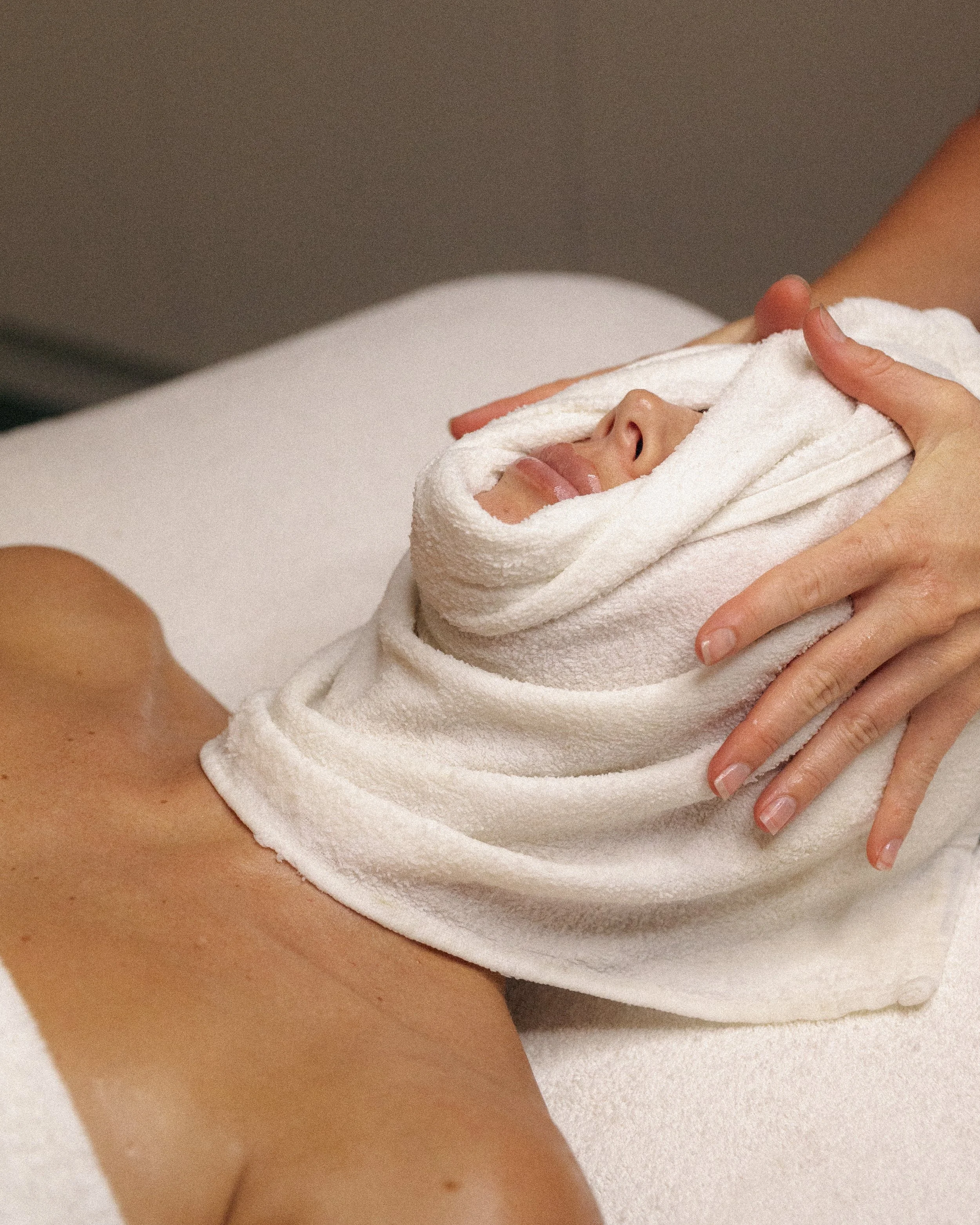 Person receiving a facial treatment with a towel wrapped around their face in a spa setting.