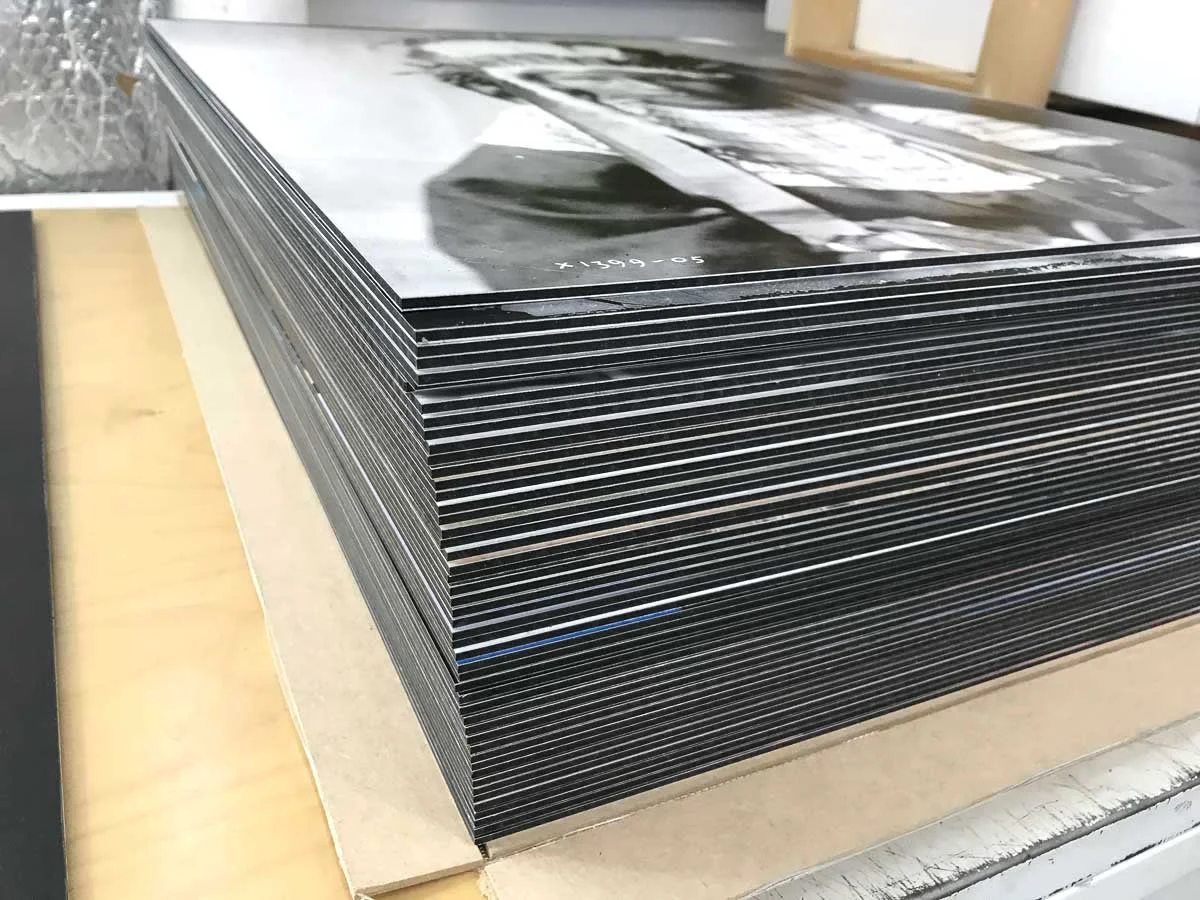 Stack of photographs or prints with black and white images, placed on a wooden surface.