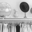 Clothing rack with hanging white shirts in a minimalist store, with round mirrors and vases in the background.