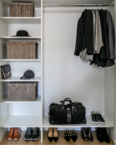 An organized closet with shelves holding baskets, hats, and accessories, and a hanging rod with jackets and scarves, with shoes on the floor.