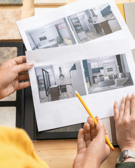 Person holding architectural plans or interior design photos of a modern kitchen and living space.