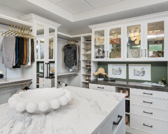 A walk-in closet with organized shelves, hanging clothes, and a marble countertop island.